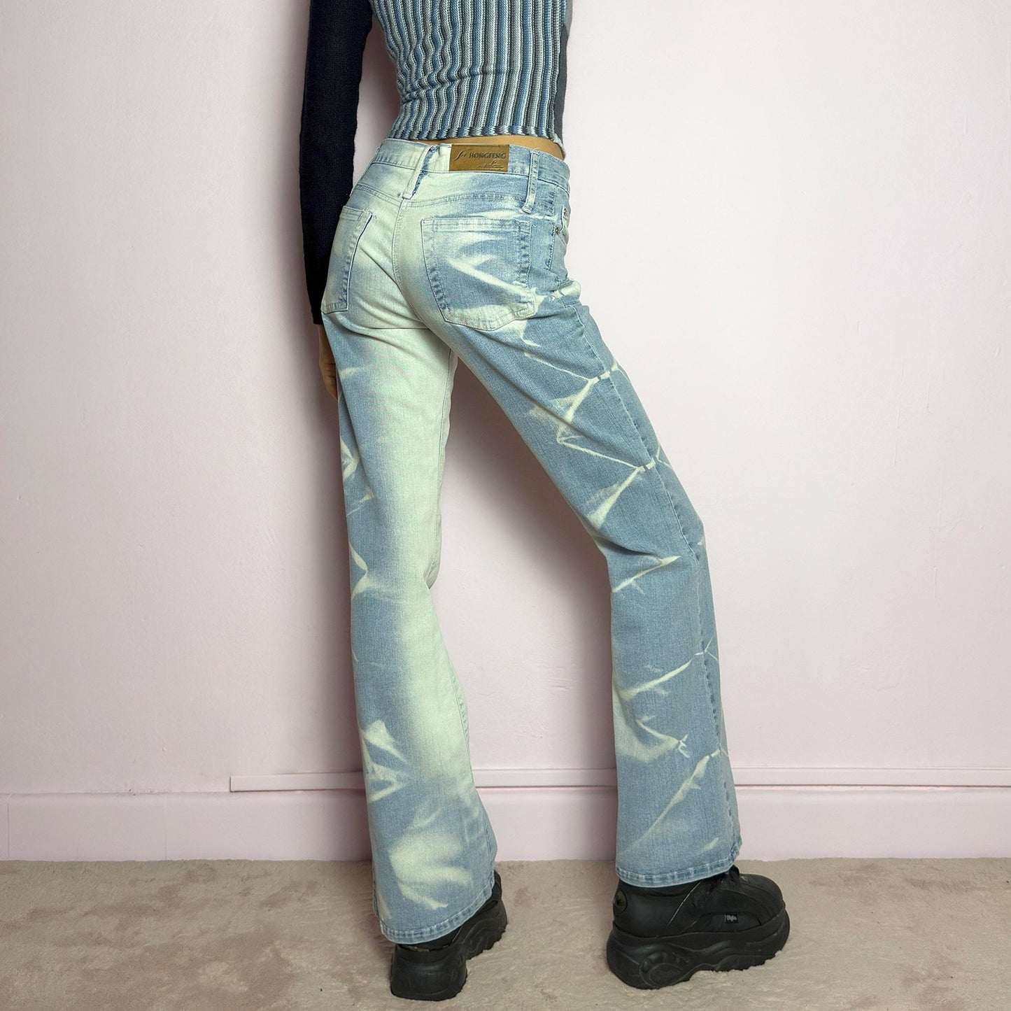 The Y2K Bleached Flare Jeans are a vintage 2000s statement piece featuring a light-wash denim with a bold bleached abstract pattern for a deconstructed, experimental look. Designed with a flattering mid-rise fit, flared legs, button and zipper closure, and pockets, these jeans are a perfect blend of edgy and playful aesthetics. Ideal for standout casual outfits. adult world shop