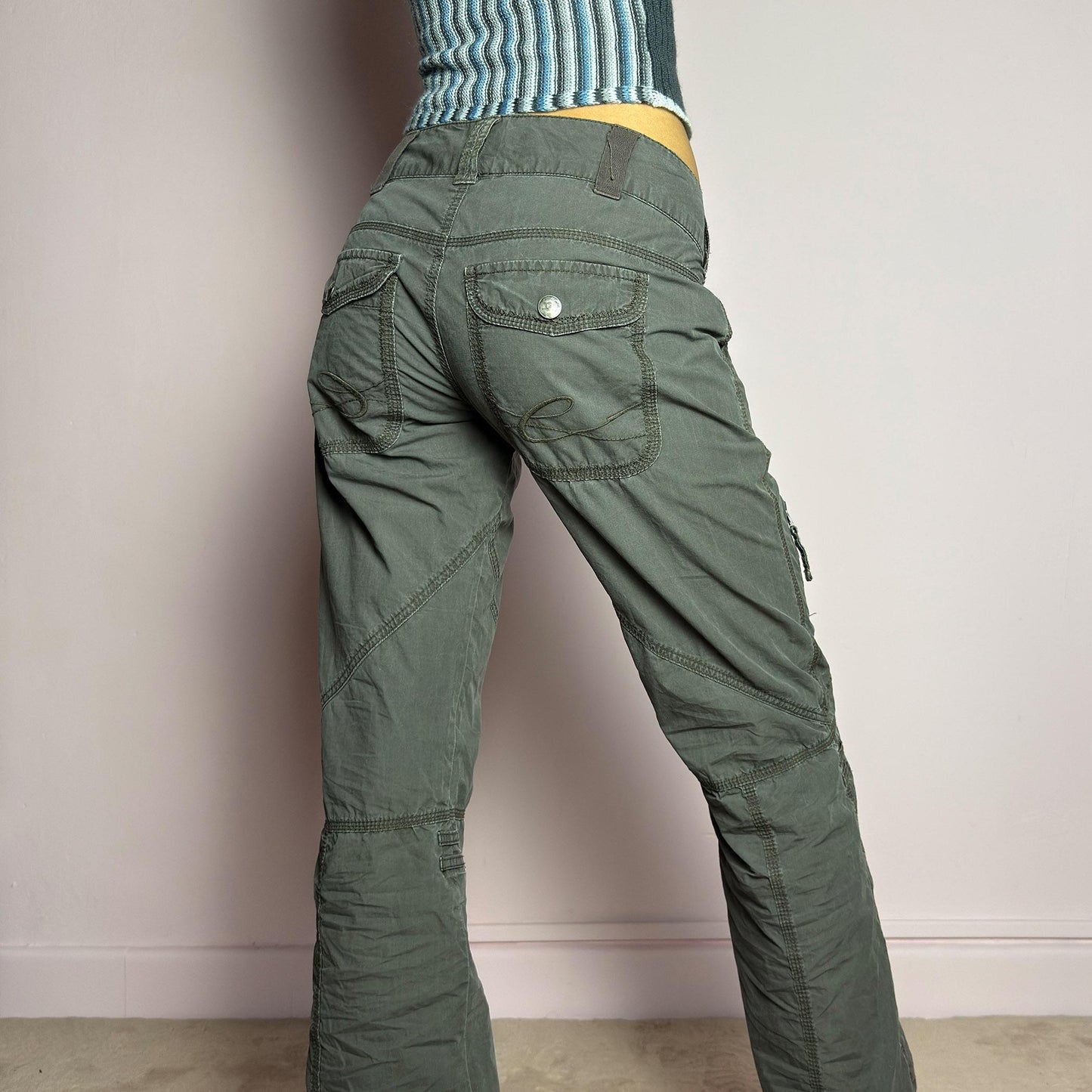 The Y2K Low-Rise Cargo Pants are a vintage 2000s piece featuring a washed gray tone with contrast stitching. Designed with a low-rise fit, button and zipper closure, and multiple cargo-style pockets, these pants have panel detailing and exposed seams that enhance their utilitarian aesthetic. The cropped straight-leg cut adds a modern touch, making them perfect for grunge and streetwear-inspired outfits. adult world shop