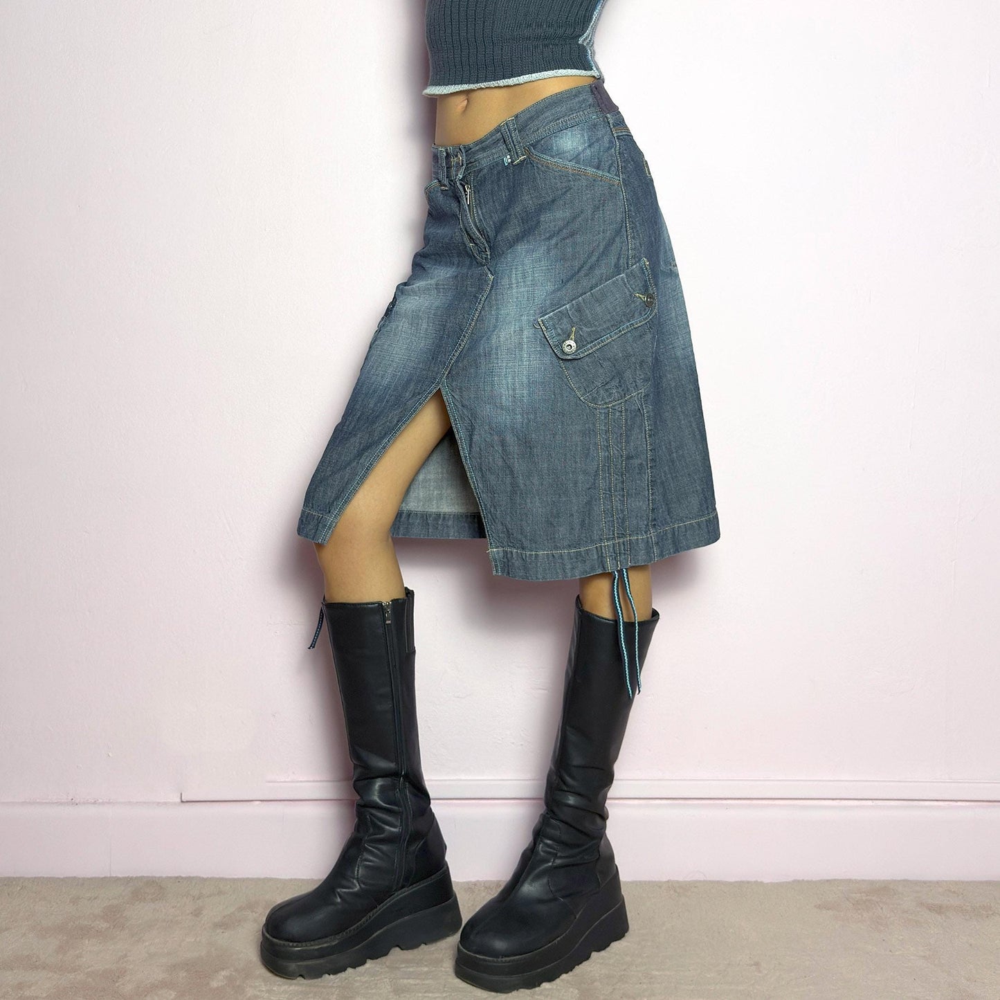 The Y2K Deconstructed Denim Midi Skirt is a vintage 2000s standout piece featuring a structured dark-wash denim fabric with contrast stitching. Designed with an asymmetrical front slit, utility-style cargo pockets, and adjustable drawstrings. Finished with a button and zipper closure, belt loops, and a mid-length silhouette, it's perfect for effortless grunge and utilitarian-inspired outfits. adult world shop