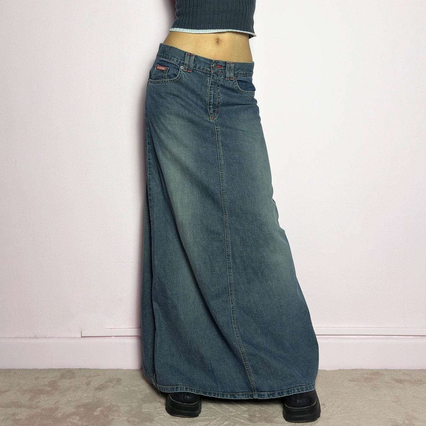 The Y2K Denim Maxi Skirt is a vintage 2000s essential featuring a structured denim fabric in a classic blue wash with subtle fading details. Designed with a mid-rise fit, button and zipper closure, and functional pockets, this skirt offers a sleek yet relaxed silhouette. The back slit adds ease of movement, making it perfect for casual everyday wear. adult world shop