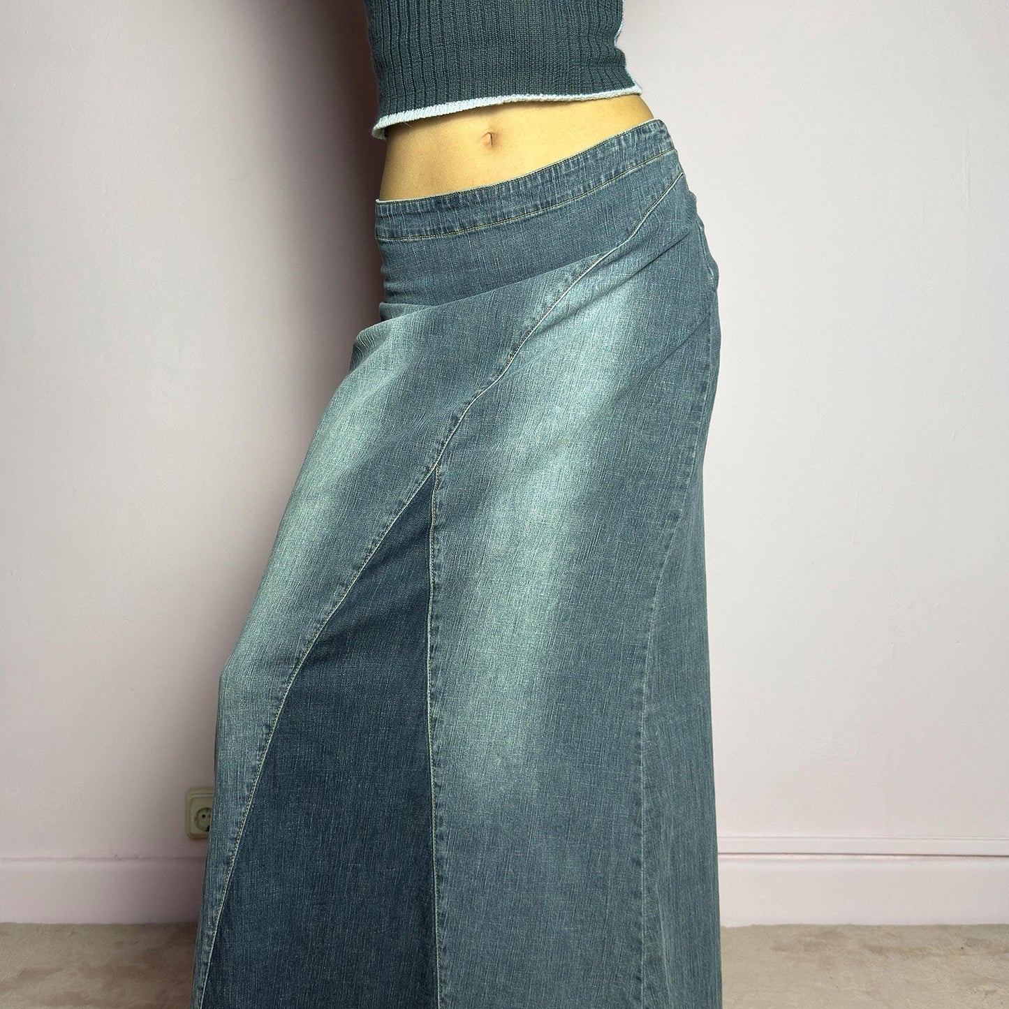 The Y2K Denim Paneled Maxi Skirt is a vintage 2000s piece featuring a unique paneled design with contrast wash details. Crafted from structured stretchy denim, this skirt offers a flattering mid-rise fit with a sleek, flared silhouette. Designed with a back zipper closure and a subtle back slit for ease of movement, it's perfect for casual streetwear outfits. adult world shop