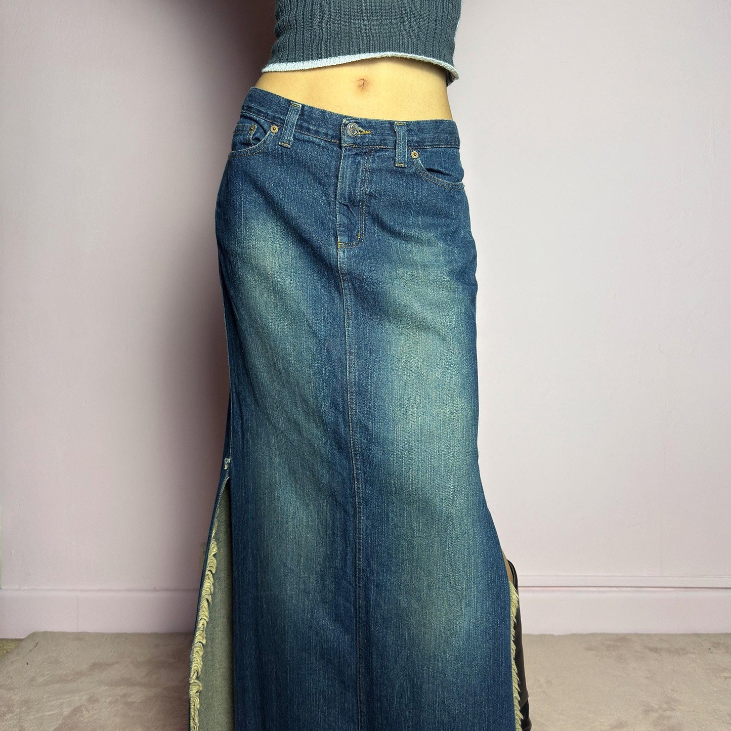 The Y2K Denim Side Slit Maxi Skirt is a vintage 2000s statement piece featuring a structured mid-rise fit and a sleek, elongated silhouette. Designed with frayed side slit details, a button and zipper closure, and classic five-pocket styling, this skirt is perfect for casual streetwear looks. adult world shop