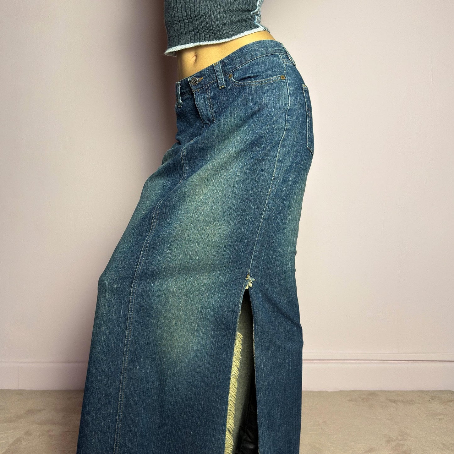 The Y2K Denim Side Slit Maxi Skirt is a vintage 2000s statement piece featuring a structured mid-rise fit and a sleek, elongated silhouette. Designed with frayed side slit details, a button and zipper closure, and classic five-pocket styling, this skirt is perfect for casual streetwear looks. adult world shop