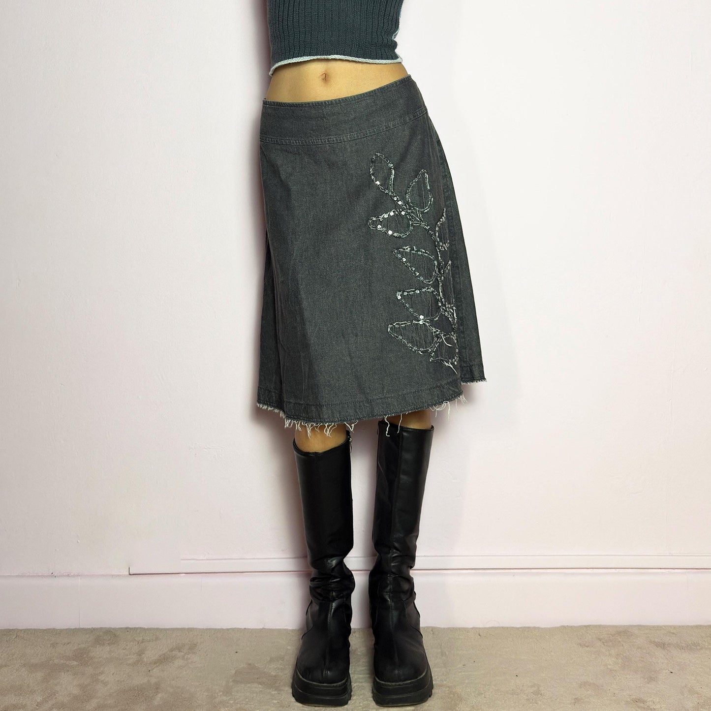 The Y2K Denim Gray Midi Skirt is a vintage 2000s piece featuring a faded gray wash, raw hem, and a unique floral sequin embroidery design. Crafted from structured denim, this skirt has an A-line silhouette that drapes effortlessly. Designed with a back zipper closure, the unfinished hem adds a deconstructed, edgy touch, making it perfect for casual outfits. adult world shop