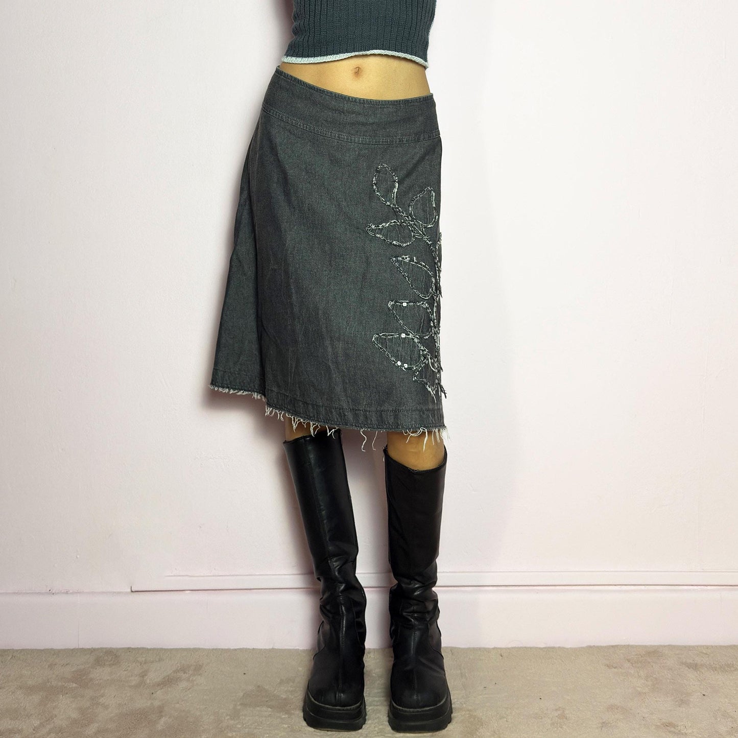 The Y2K Denim Gray Midi Skirt is a vintage 2000s piece featuring a faded gray wash, raw hem, and a unique floral sequin embroidery design. Crafted from structured denim, this skirt has an A-line silhouette that drapes effortlessly. Designed with a back zipper closure, the unfinished hem adds a deconstructed, edgy touch, making it perfect for casual outfits. adult world shop