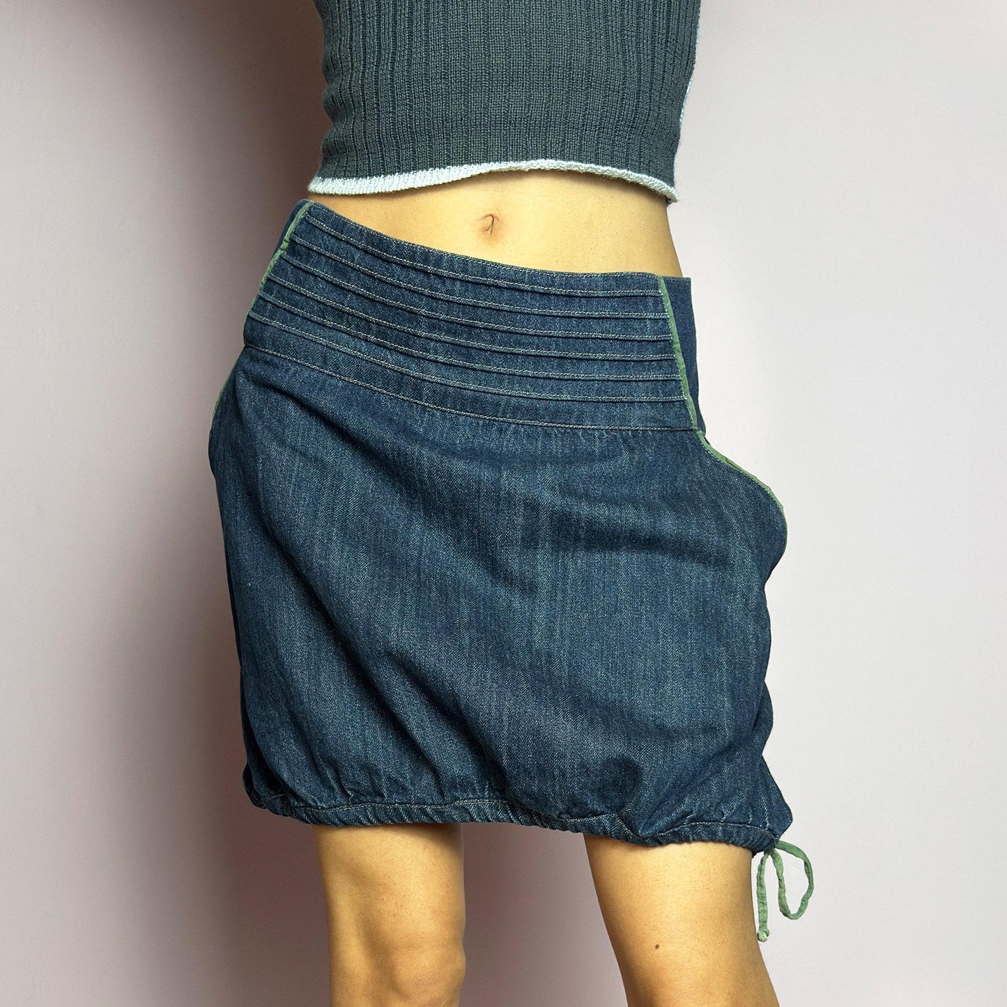The Y2K Denim Bubble Mini Skirt is a vintage 2000s piece featuring a dark wash denim with unique structured pleating at the waist. Designed with an adjustable bubble hem with drawstrings for a customizable fit, this skirt blends playful and edgy aesthetics. It also includes a side zipper closure. Perfect for statement streetwear looks. adult world shop