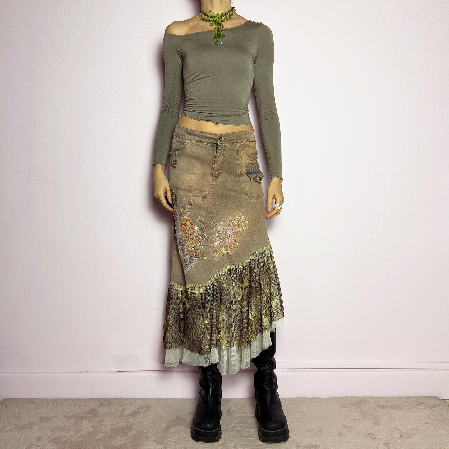 The Y2K Asymmetric Ruffle Midi Skirt is a vintage 2000s statement piece featuring a stretchy distressed tan denim base adorned with intricate beaded floral embroidery and sequin details. Designed with an asymmetric layered ruffle hem made of sheer lace and mesh with a metallic floral pattern, this skirt creates a dreamy, deconstructed aesthetic. It includes a button and zipper closure, belt loops, and pockets. adult world shop