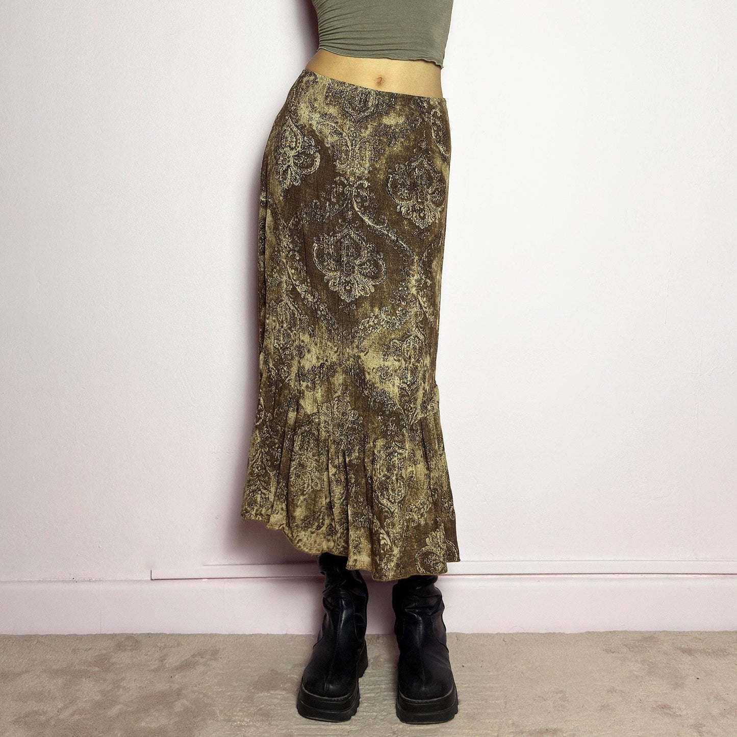 The Y2K Brown Paisley Midi Skirt is a vintage 2000s piece featuring a baroque-inspired paisley print. Designed with an earthy, whimsical aesthetic, this skirt has a flowy silhouette with subtle ruffle tiered details at the hem. It features a side zipper closure with an elastic waist. Perfect for grunge and bohemian-inspired outfits. adult world shop