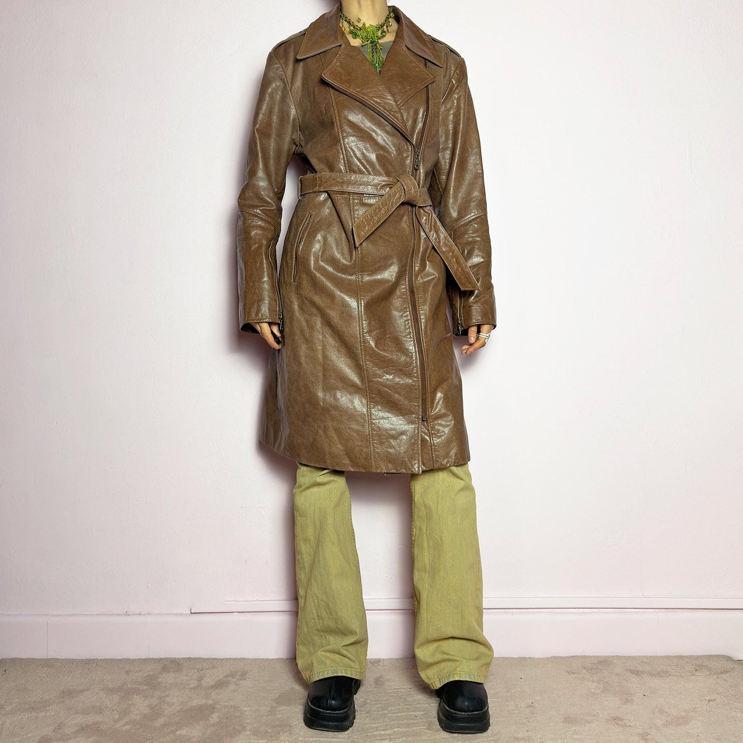 The Y2K Long Brown Leather Coat is a heavy, structured vintage 2000s piece crafted from genuine leather. It features an asymmetrical zip closure, a wide lapel collar, and a belted waist for a cinched silhouette. The coat includes pockets and a smooth lining for comfort. With its durable construction and timeless design, this vintage long leather coat is perfect for edgy streetwear or sophisticated layering. adult world shop