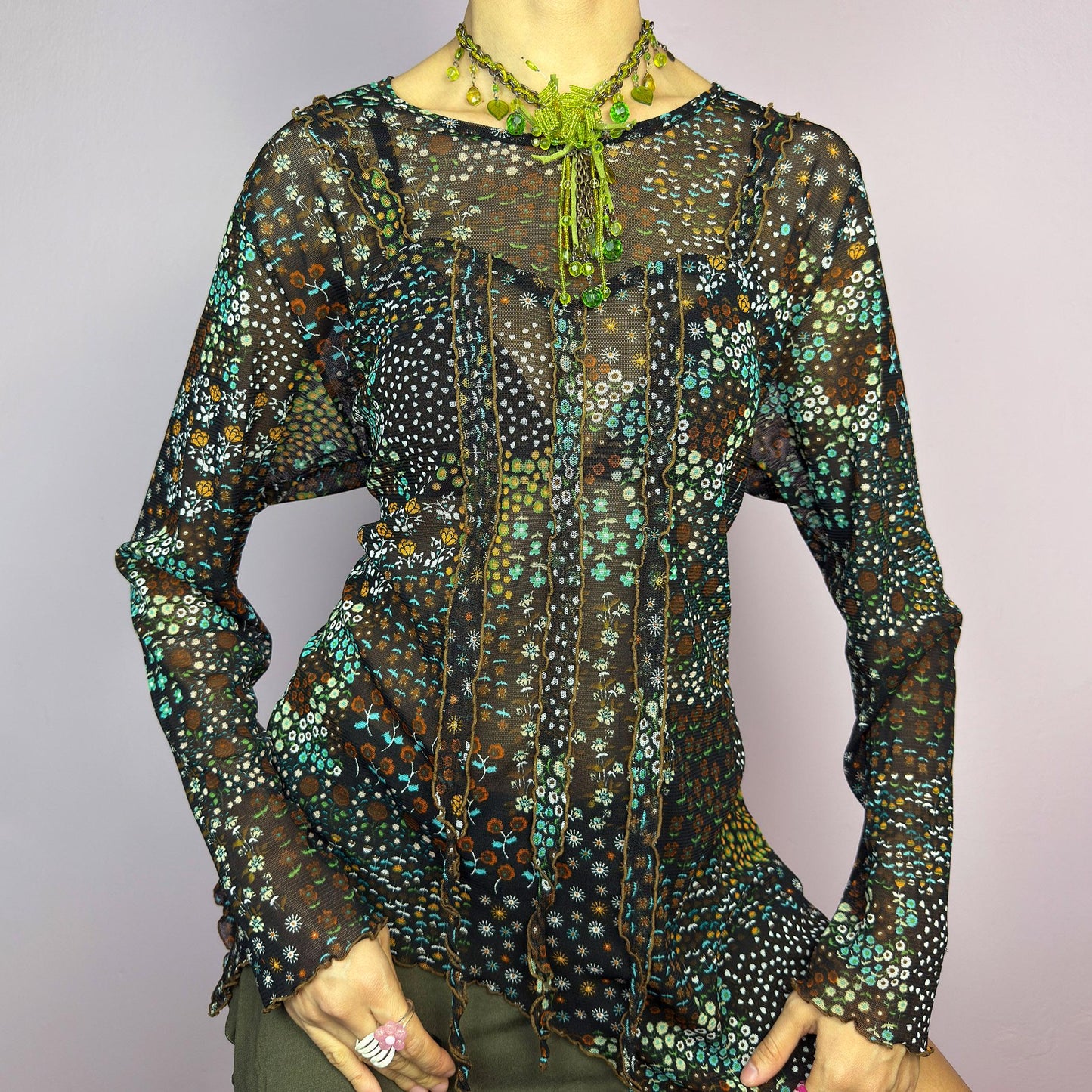 The Y2K Black Asymmetric Mesh Top is a vintage 2000s statement piece featuring semi-sheer mesh fabric with a floral and geometric print. Designed with an edgy asymmetric cut and delicate lettuce hem detailing, this top embodies a deconstructed aesthetic with a fairy grunge-inspired touch. The lightweight, stretchy fabric makes it perfect for layering, making it an ideal choice for summer avant-garde outfits. adult world shop