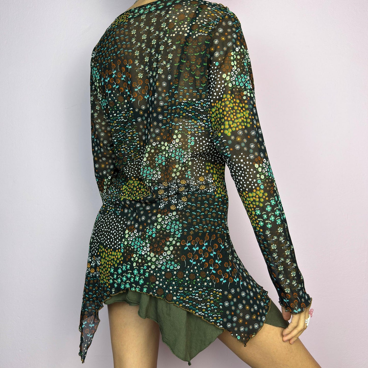 The Y2K Black Asymmetric Mesh Top is a vintage 2000s statement piece featuring semi-sheer mesh fabric with a floral and geometric print. Designed with an edgy asymmetric cut and delicate lettuce hem detailing, this top embodies a deconstructed aesthetic with a fairy grunge-inspired touch. The lightweight, stretchy fabric makes it perfect for layering, making it an ideal choice for summer avant-garde outfits. adult world shop
