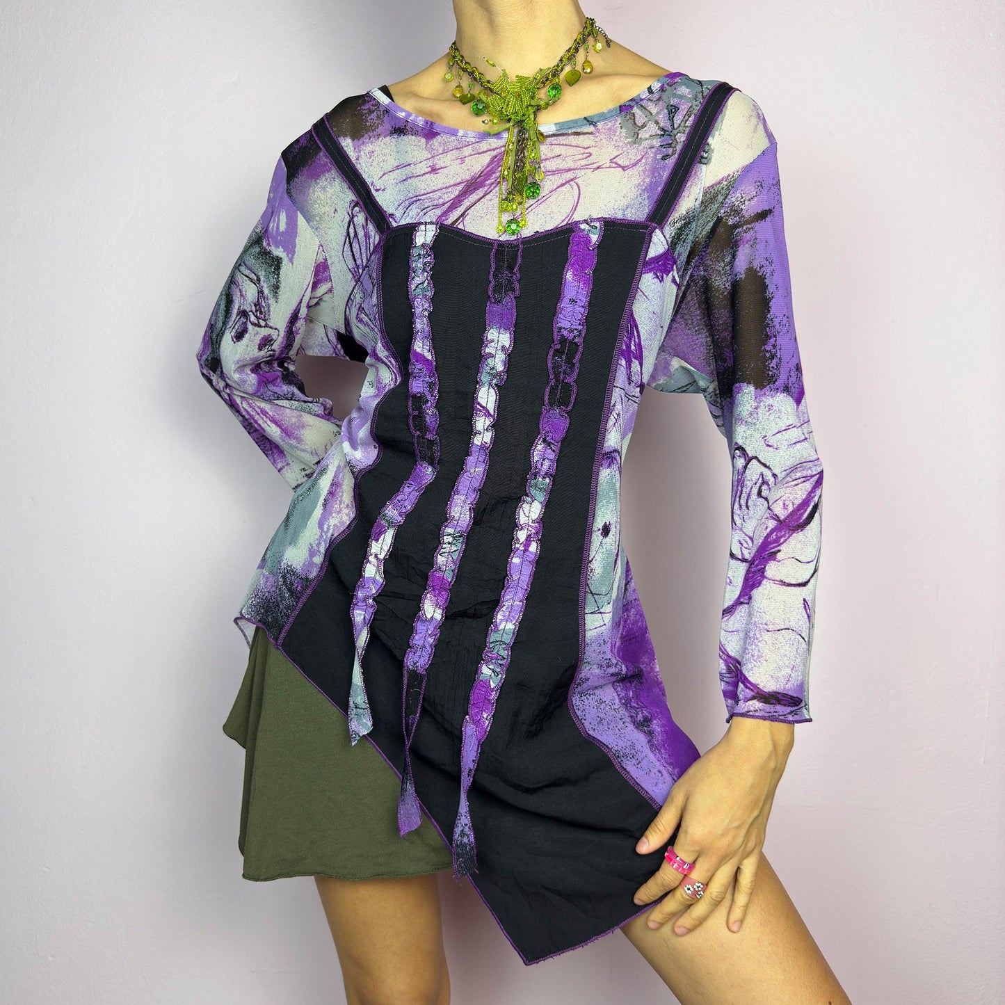 The Y2K Mesh Asymmetric Black Top is a vintage 2000s piece featuring a semi-sheer mesh fabric with an abstract purple, black, and white print. Designed with three quarter sleeves and contrast paneling and exposed seams, this top has a deconstructed, edgy aesthetic. The asymmetric hem and raw cut details add a unique touch, making it perfect for grunge or fairycore-inspired outfits. Lightweight and stretchy, ideal for layering and statement looks. adult world shop