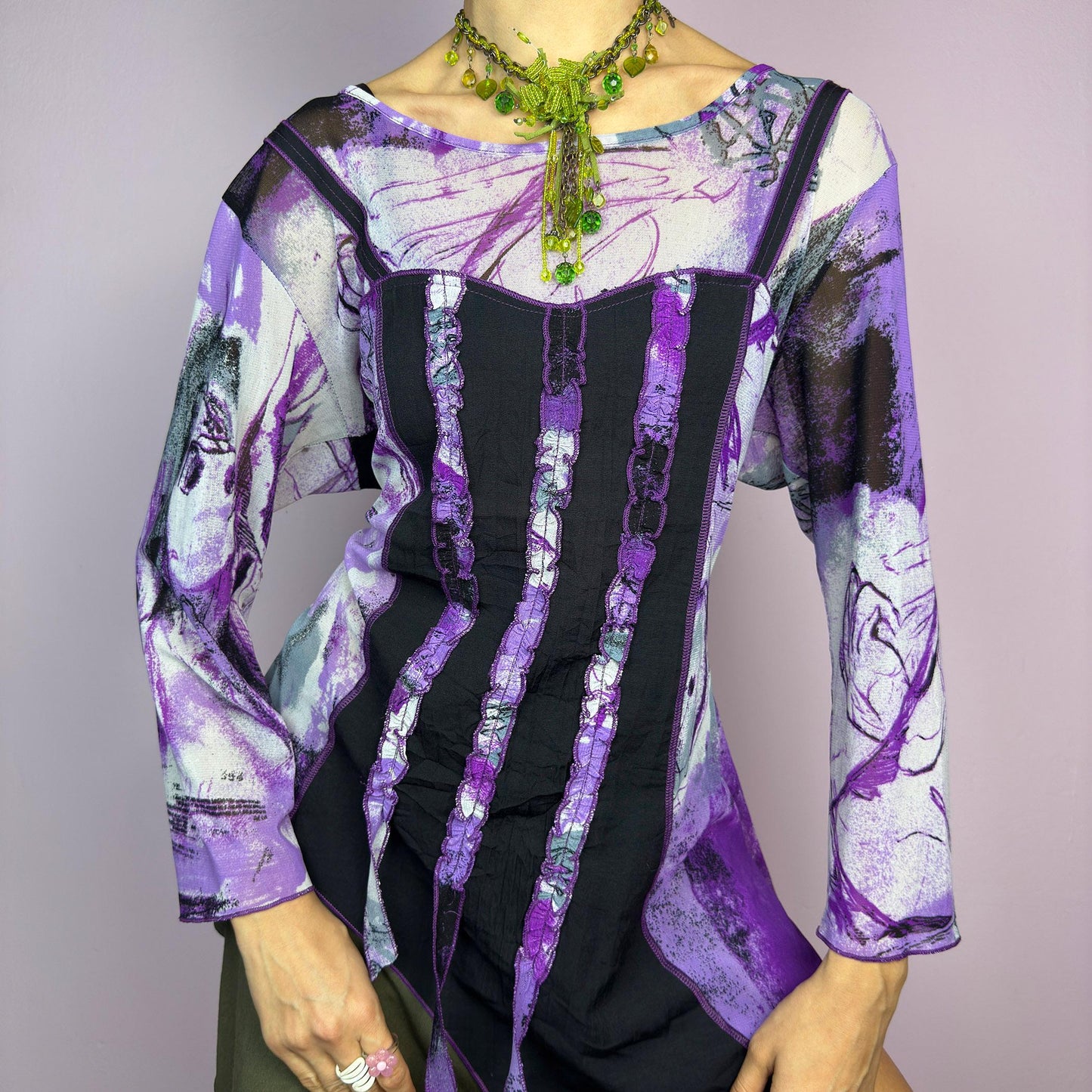 The Y2K Mesh Asymmetric Black Top is a vintage 2000s piece featuring a semi-sheer mesh fabric with an abstract purple, black, and white print. Designed with three quarter sleeves and contrast paneling and exposed seams, this top has a deconstructed, edgy aesthetic. The asymmetric hem and raw cut details add a unique touch, making it perfect for grunge or fairycore-inspired outfits. Lightweight and stretchy, ideal for layering and statement looks. adult world shop