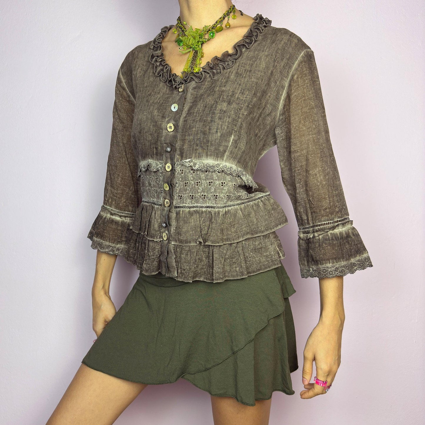 The Y2K Brown Ruffle Frill Blouse is a vintage 2000s piece featuring a faded brown wash with delicate lace trims and tiered ruffle details for a romantic, fairy-grunge aesthetic. Designed with a button-up front, 3/4 bell sleeves, this blouse blends cottagecore and bohemian elements effortlessly. The soft, lightweight fabric makes it perfect for dreamy summer outfits. adult world shop