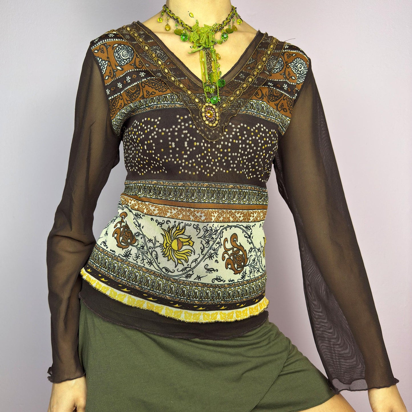The Y2K Brown Bell Sleeve Mesh Top is a vintage 2000s piece featuring a semi-sheer mesh fabric with baroque and floral-inspired prints. Designed with flared bell sleeves, a fitted silhouette, and a layered hem, this top embodies a dreamy bohemian aesthetic. The lightweight and stretchy fabric make it perfect for ethereal, fairy-grunge looks. adult world shop
