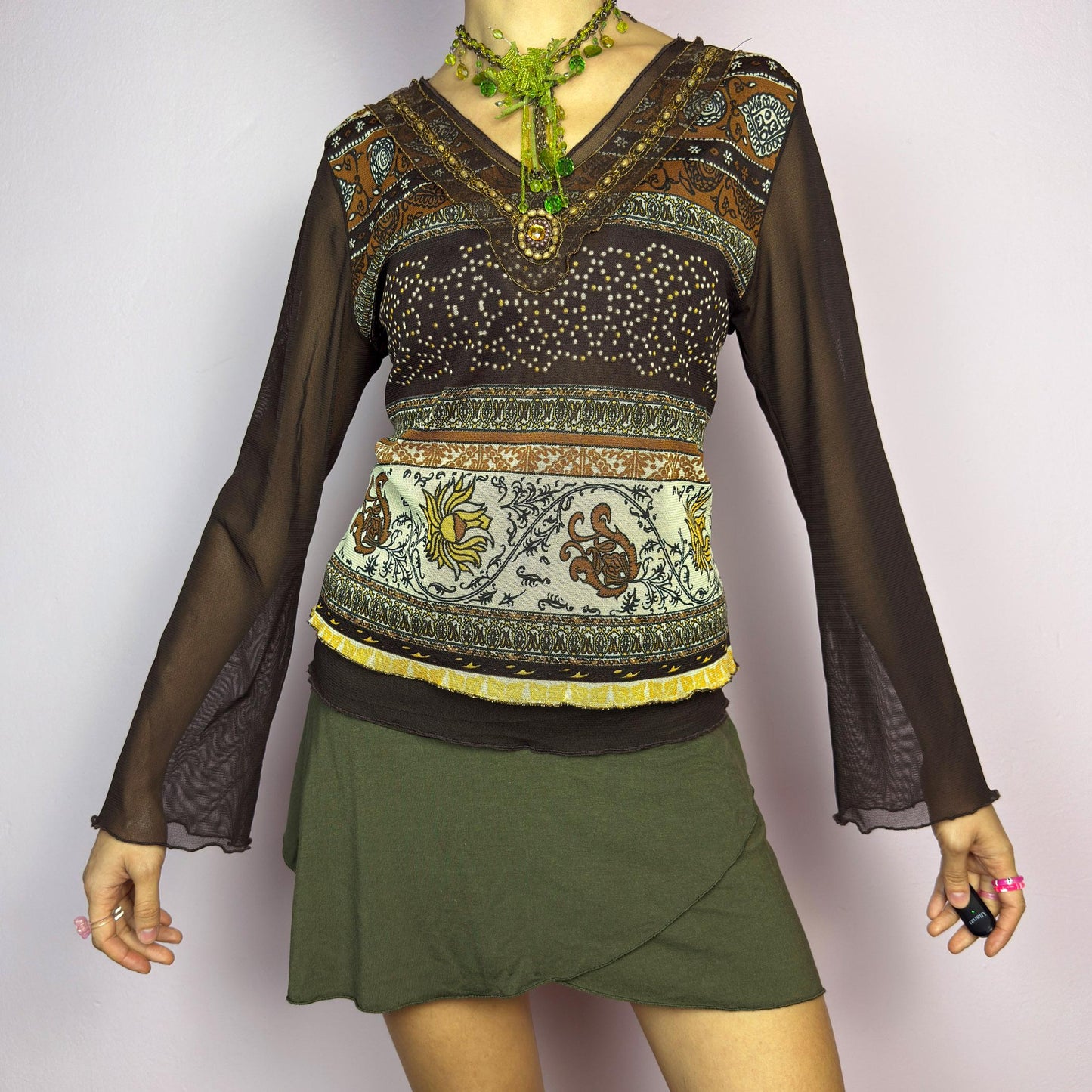 The Y2K Brown Bell Sleeve Mesh Top is a vintage 2000s piece featuring a semi-sheer mesh fabric with baroque and floral-inspired prints. Designed with flared bell sleeves, a fitted silhouette, and a layered hem, this top embodies a dreamy bohemian aesthetic. The lightweight and stretchy fabric make it perfect for ethereal, fairy-grunge looks. adult world shop