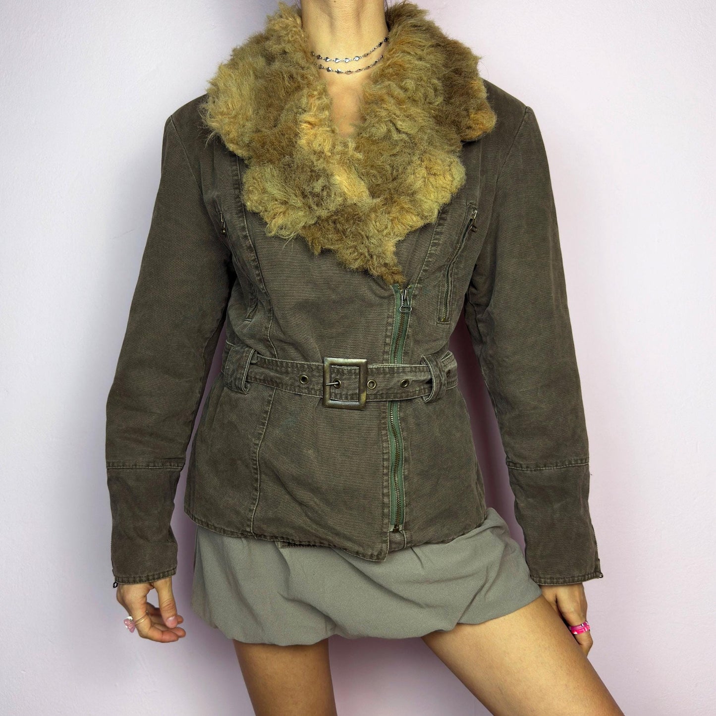 The Y2K Khaki Belted Jacket is a vintage 2000s piece featuring a structured fit with rugged utility-inspired details. Designed with padded shoulders for a strong silhouette, an oversized plush faux-shearling collar, asymmetric zip closure, and an adjustable waist belt for a cinched look. The washed khaki tone and distressed finish add to its edgy, worn-in appeal, making it perfect for grunge or military-inspired winter outfits. A outerwear piece for layering in colder seasons. adult world shop