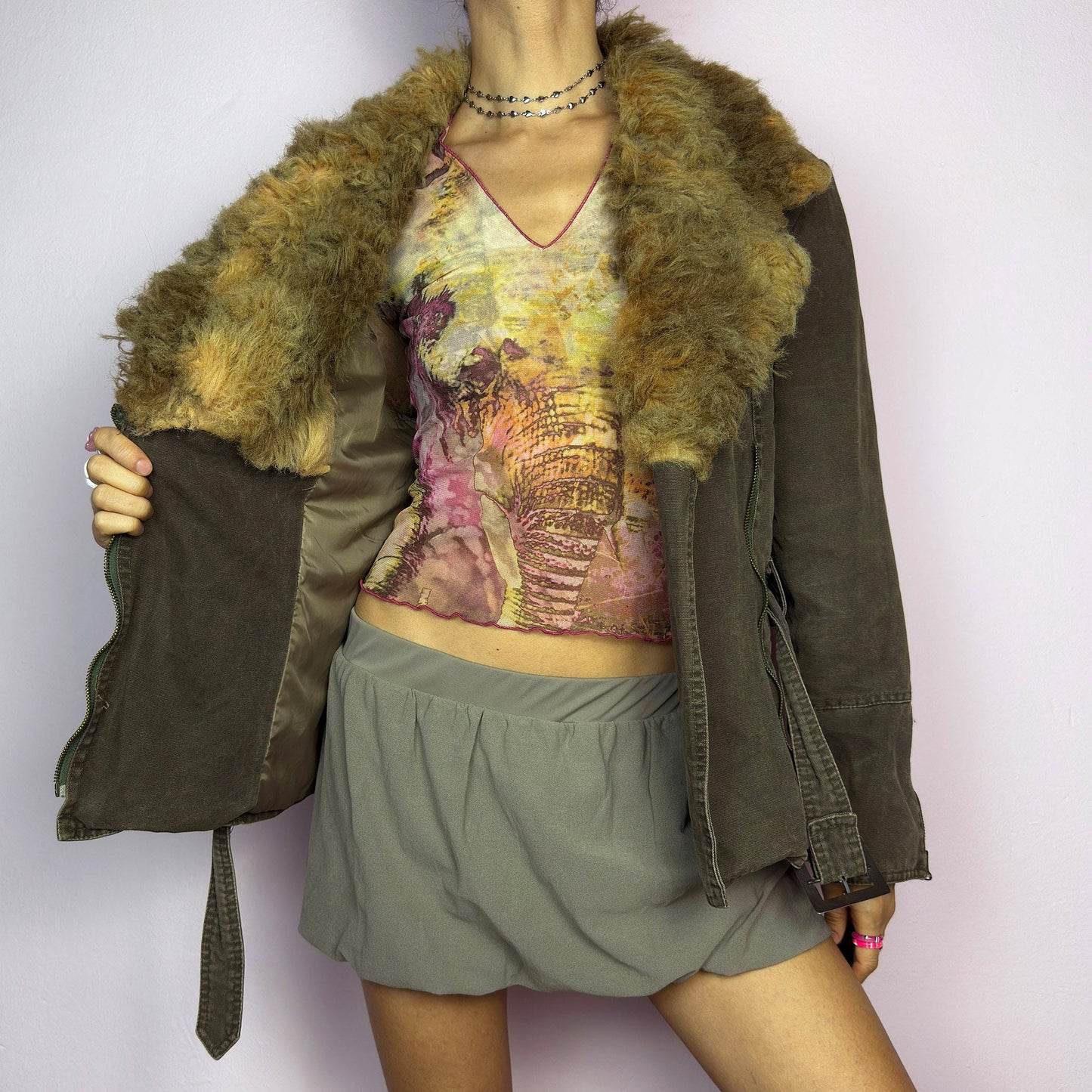 The Y2K Khaki Belted Jacket is a vintage 2000s piece featuring a structured fit with rugged utility-inspired details. Designed with padded shoulders for a strong silhouette, an oversized plush faux-shearling collar, asymmetric zip closure, and an adjustable waist belt for a cinched look. The washed khaki tone and distressed finish add to its edgy, worn-in appeal, making it perfect for grunge or military-inspired winter outfits. A outerwear piece for layering in colder seasons. adult world shop