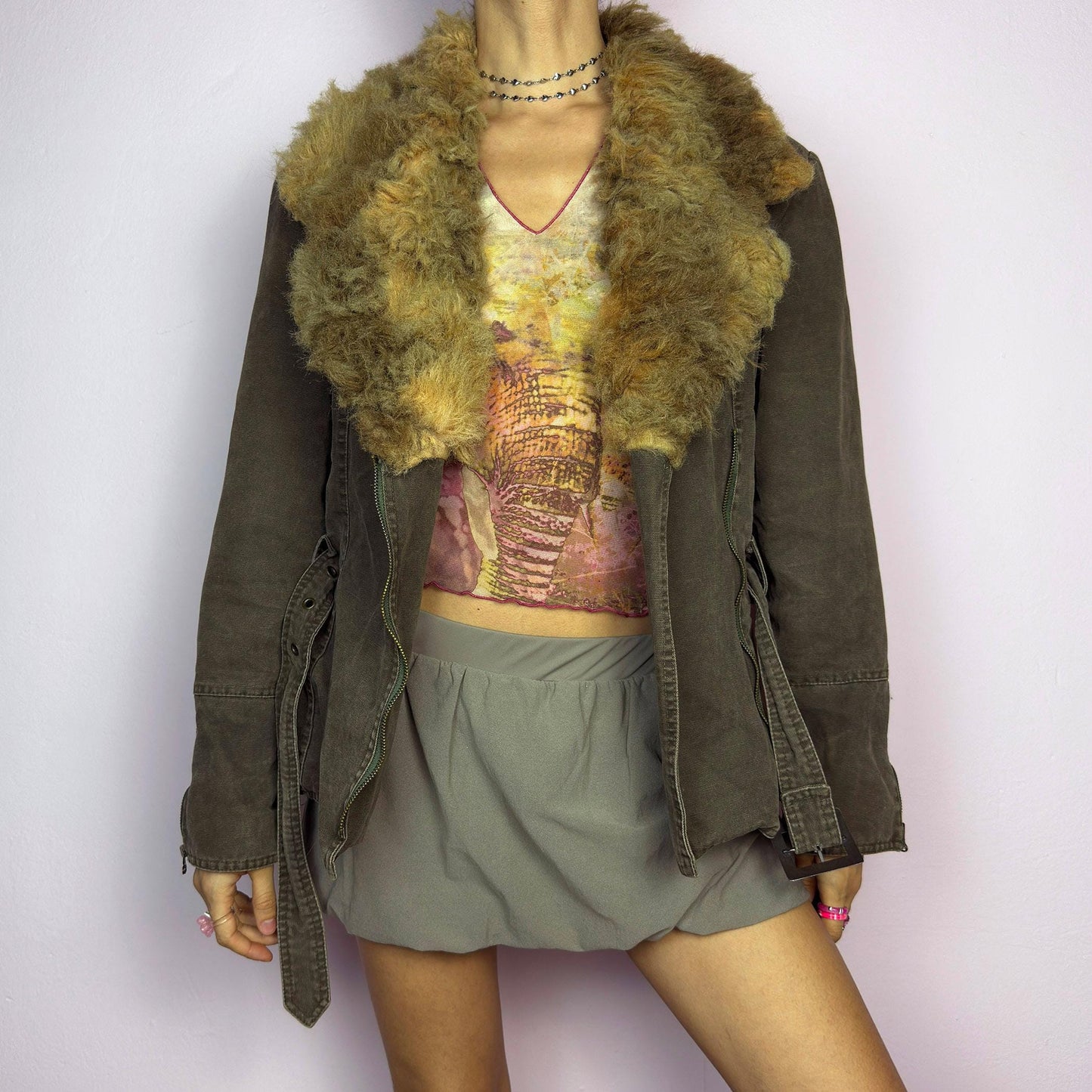 The Y2K Khaki Belted Jacket is a vintage 2000s piece featuring a structured fit with rugged utility-inspired details. Designed with padded shoulders for a strong silhouette, an oversized plush faux-shearling collar, asymmetric zip closure, and an adjustable waist belt for a cinched look. The washed khaki tone and distressed finish add to its edgy, worn-in appeal, making it perfect for grunge or military-inspired winter outfits. A outerwear piece for layering in colder seasons. adult world shop