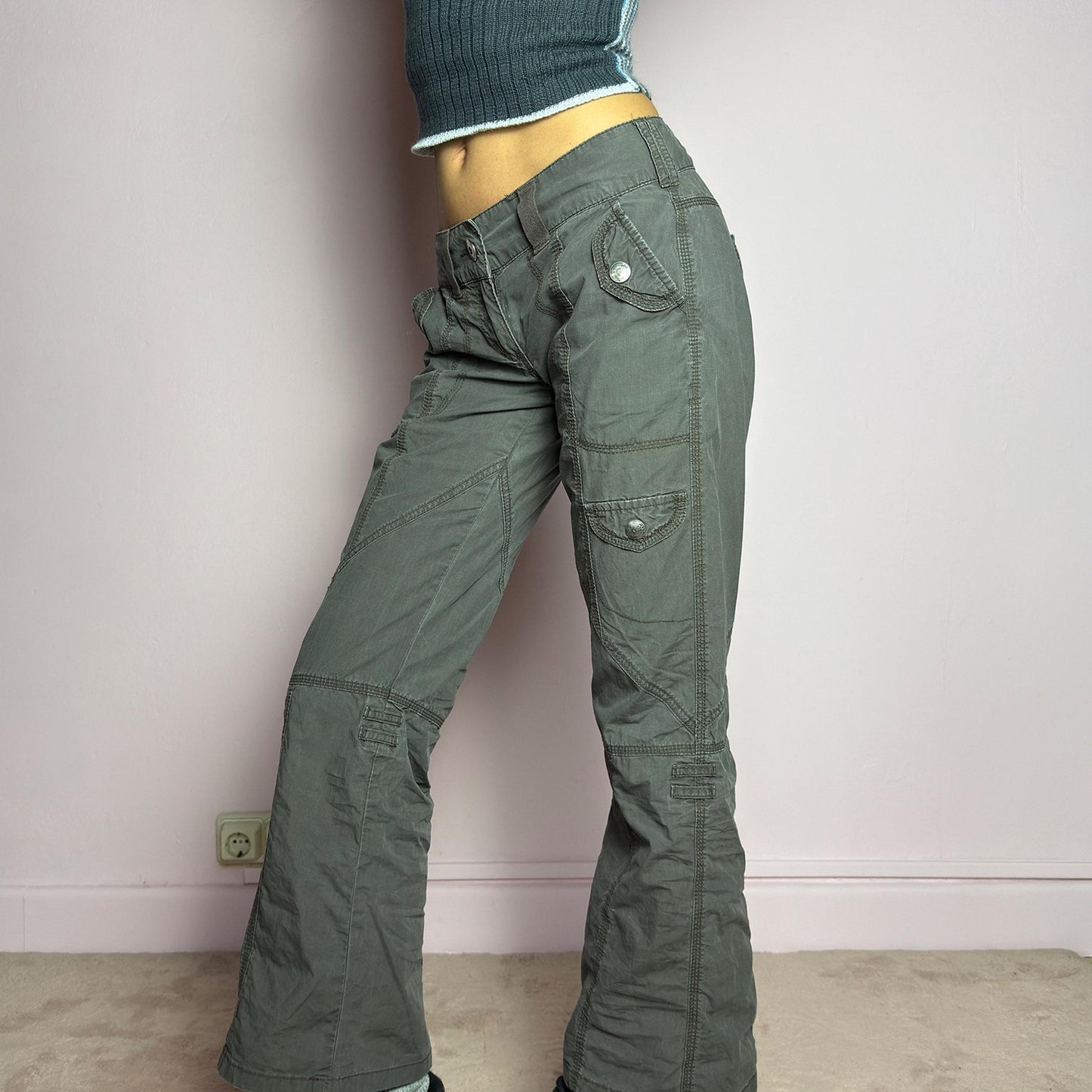 The Y2K Low-Rise Cargo Pants are a vintage 2000s piece featuring a washed gray tone with contrast stitching. Designed with a low-rise fit, button and zipper closure, and multiple cargo-style pockets, these pants have panel detailing and exposed seams that enhance their utilitarian aesthetic. The cropped straight-leg cut adds a modern touch, making them perfect for grunge and streetwear-inspired outfits. adult world shop