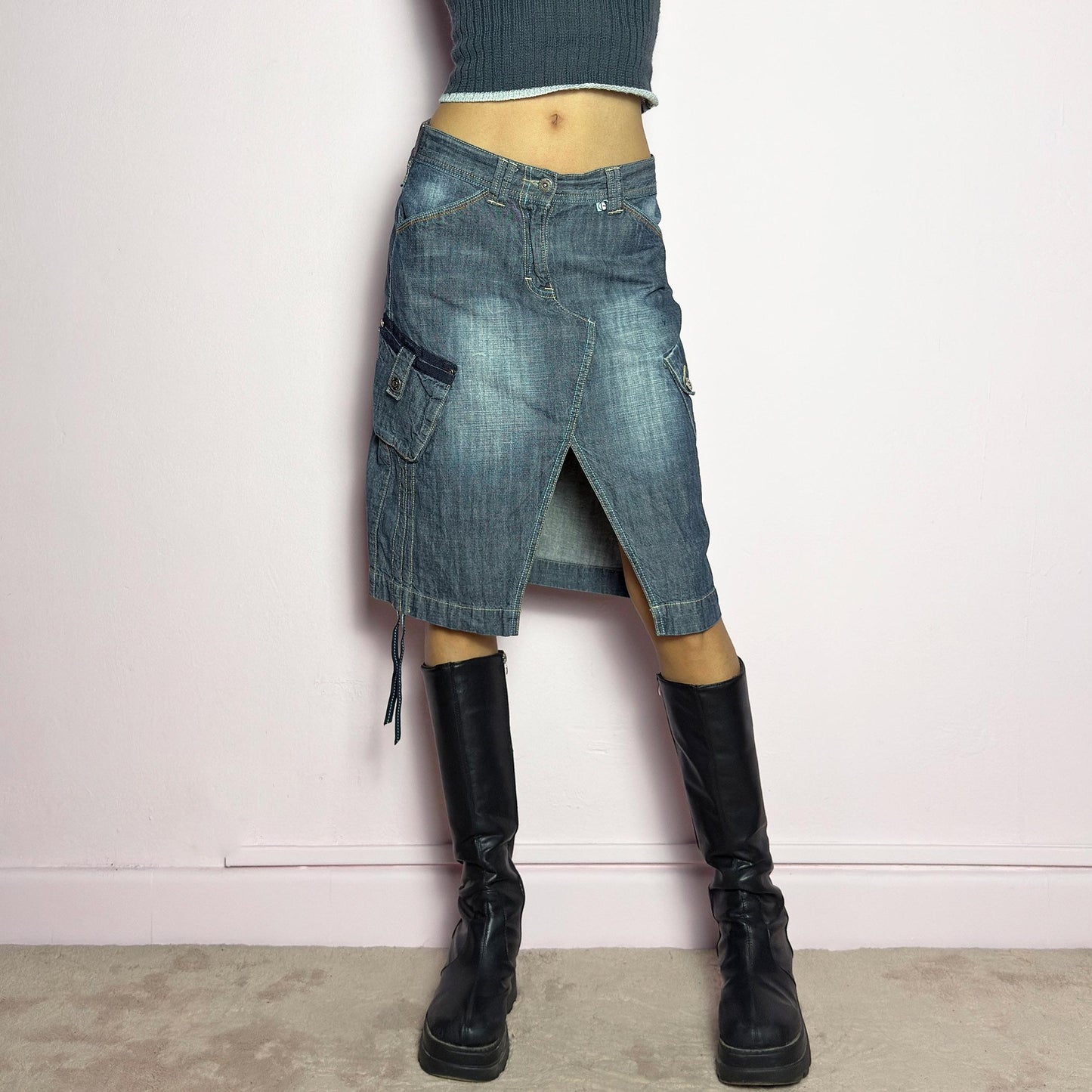 The Y2K Deconstructed Denim Midi Skirt is a vintage 2000s standout piece featuring a structured dark-wash denim fabric with contrast stitching. Designed with an asymmetrical front slit, utility-style cargo pockets, and adjustable drawstrings. Finished with a button and zipper closure, belt loops, and a mid-length silhouette, it's perfect for effortless grunge and utilitarian-inspired outfits. adult world shop