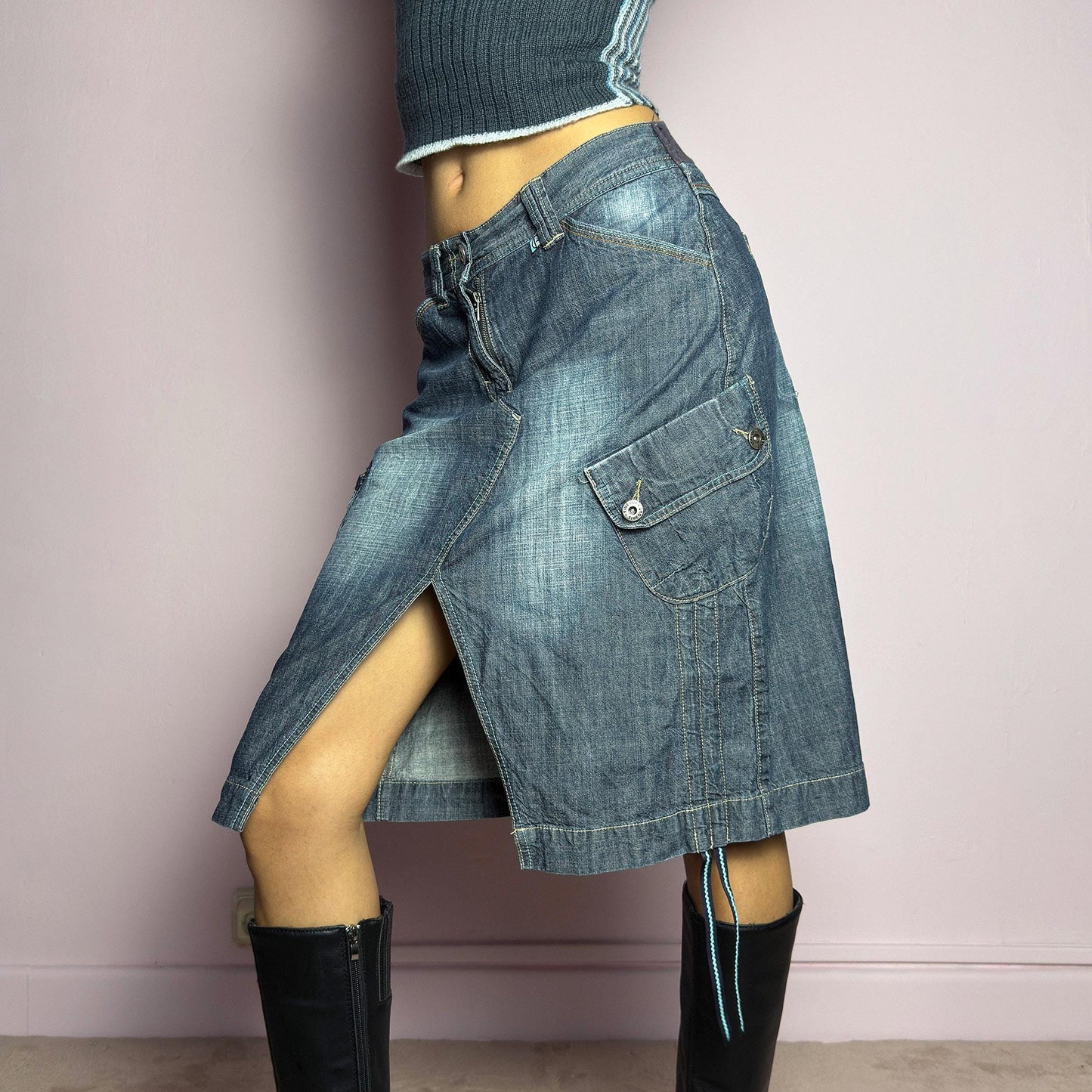 The Y2K Deconstructed Denim Midi Skirt is a vintage 2000s standout piece featuring a structured dark-wash denim fabric with contrast stitching. Designed with an asymmetrical front slit, utility-style cargo pockets, and adjustable drawstrings. Finished with a button and zipper closure, belt loops, and a mid-length silhouette, it's perfect for effortless grunge and utilitarian-inspired outfits. adult world shop