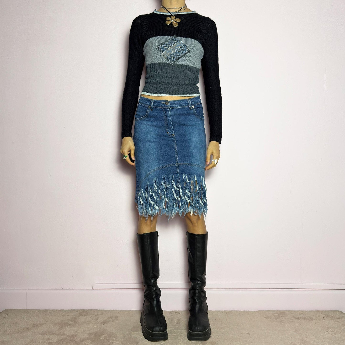 The Y2K Denim Distressed Midi Skirt is a vintage 2000s statement piece featuring a deconstructed look with dramatic distressed fringe details along the hem and back pockets. Designed with a stretchy structured denim fabric, a mid-rise fit, button and zipper closure, and pockets, this skirt blends edgy and casual aesthetics. adult world shop