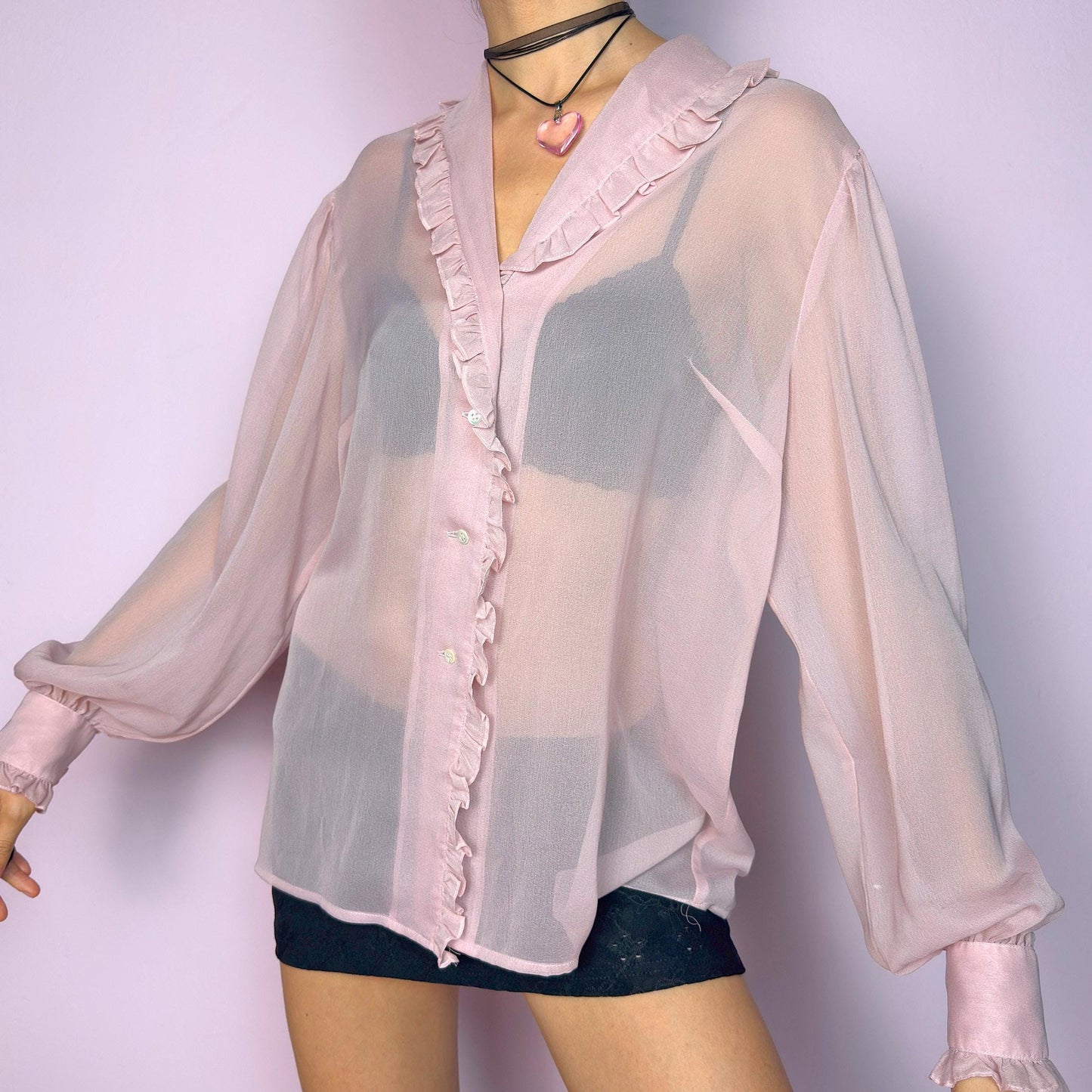 The Vintage Pink Ruffle Sheer Blouse features a romantic and ethereal silhouette with soft, see-through fabric and delicate ruffle trim along the collar and button placket. The flowy cut and voluminous sleeves with buttoned cuffs add a dreamy charm. Perfect for layering for a soft coquette aesthetic. Made in France. Excellent vintage condition. adult world shop