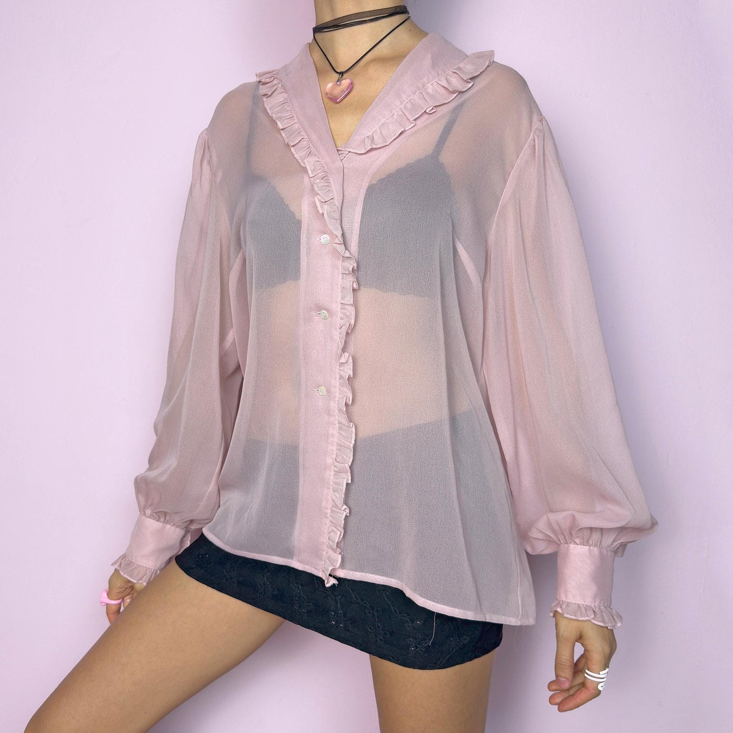 The Vintage Pink Ruffle Sheer Blouse features a romantic and ethereal silhouette with soft, see-through fabric and delicate ruffle trim along the collar and button placket. The flowy cut and voluminous sleeves with buttoned cuffs add a dreamy charm. Perfect for layering for a soft coquette aesthetic. Made in France. Excellent vintage condition. adult world shop