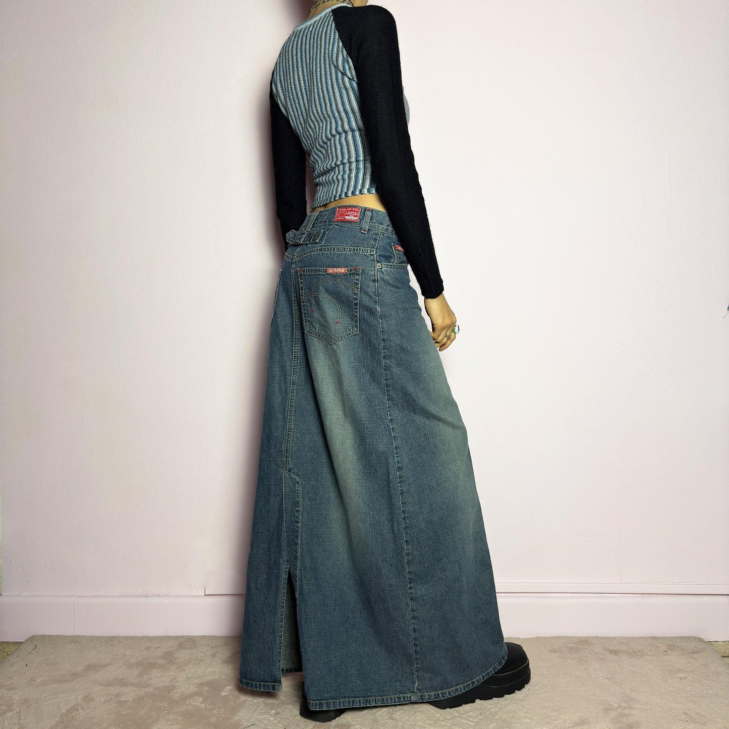 The Y2K Denim Maxi Skirt is a vintage 2000s essential featuring a structured denim fabric in a classic blue wash with subtle fading details. Designed with a mid-rise fit, button and zipper closure, and functional pockets, this skirt offers a sleek yet relaxed silhouette. The back slit adds ease of movement, making it perfect for casual everyday wear. adult world shop