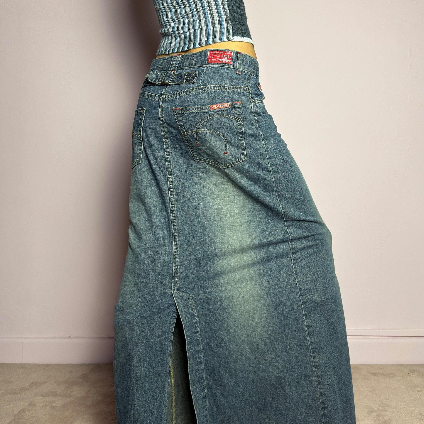 The Y2K Denim Maxi Skirt is a vintage 2000s essential featuring a structured denim fabric in a classic blue wash with subtle fading details. Designed with a mid-rise fit, button and zipper closure, and functional pockets, this skirt offers a sleek yet relaxed silhouette. The back slit adds ease of movement, making it perfect for casual everyday wear. adult world shop
