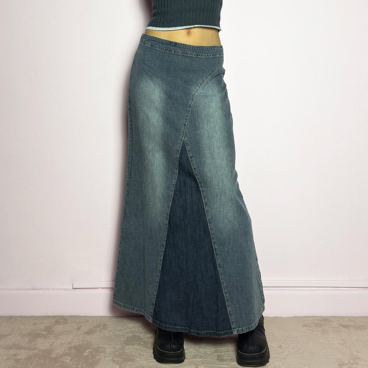 The Y2K Denim Paneled Maxi Skirt is a vintage 2000s piece featuring a unique paneled design with contrast wash details. Crafted from structured stretchy denim, this skirt offers a flattering mid-rise fit with a sleek, flared silhouette. Designed with a back zipper closure and a subtle back slit for ease of movement, it's perfect for casual streetwear outfits. adult world shop