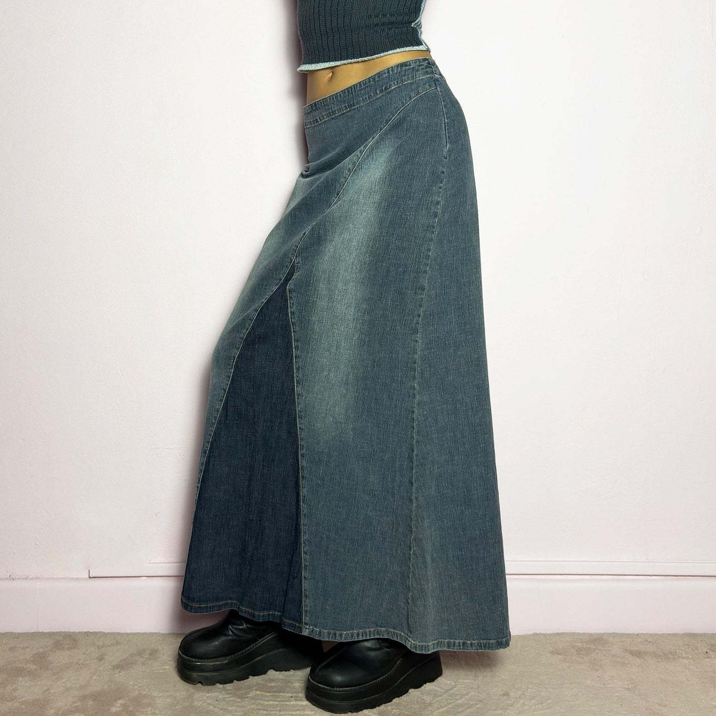 The Y2K Denim Paneled Maxi Skirt is a vintage 2000s piece featuring a unique paneled design with contrast wash details. Crafted from structured stretchy denim, this skirt offers a flattering mid-rise fit with a sleek, flared silhouette. Designed with a back zipper closure and a subtle back slit for ease of movement, it's perfect for casual streetwear outfits. adult world shop