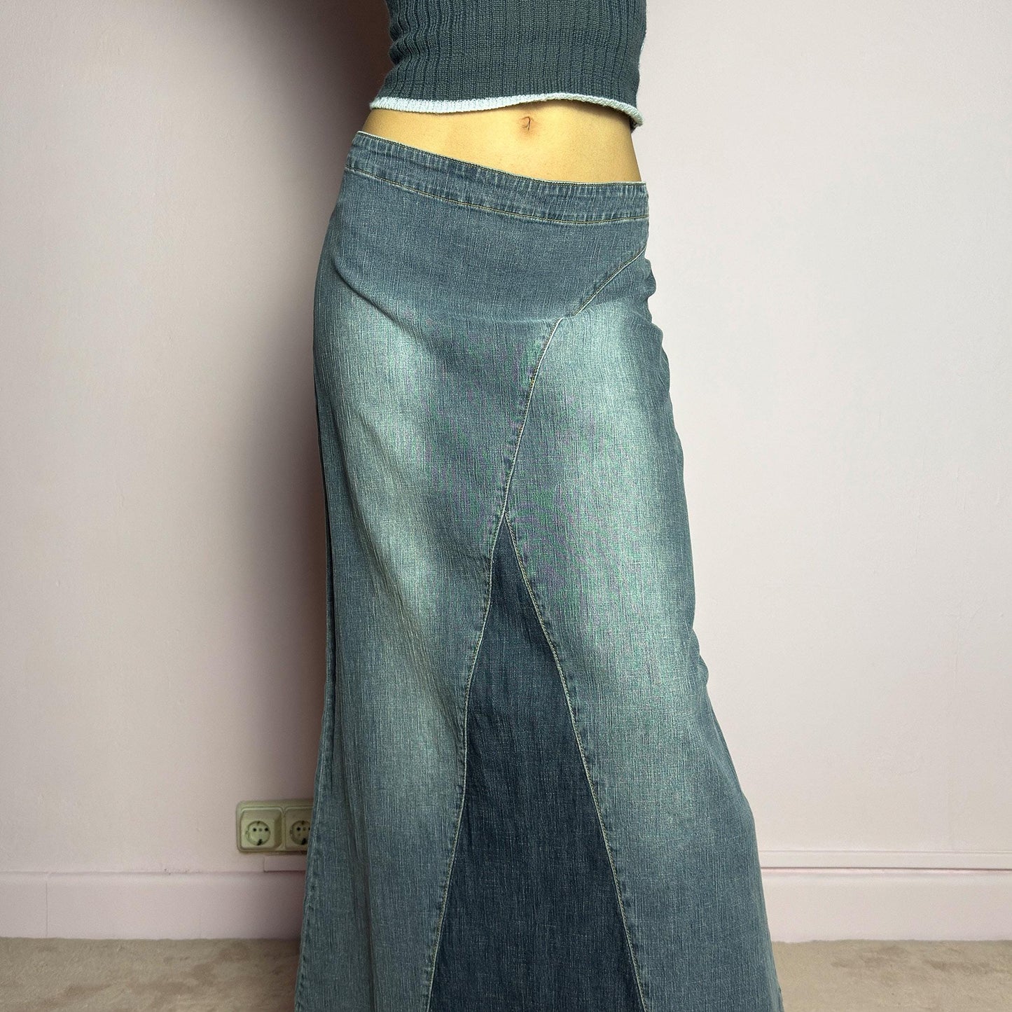 The Y2K Denim Paneled Maxi Skirt is a vintage 2000s piece featuring a unique paneled design with contrast wash details. Crafted from structured stretchy denim, this skirt offers a flattering mid-rise fit with a sleek, flared silhouette. Designed with a back zipper closure and a subtle back slit for ease of movement, it's perfect for casual streetwear outfits. adult world shop
