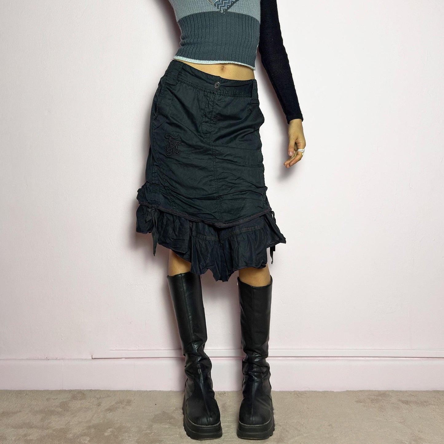 The Y2K Black Layered Skirt by Marithé François Girbaud is a vintage 2000s statement piece featuring a structured design with ruched details and ruffled layers for added texture and movement. Designed with a mid-rise fit, button and zipper closure, embroidered side detail, and an asymmetrical hem, this skirt blends edgy streetwear vibes with a playful, gothic aesthetic. Perfect for casual grunge and alternative looks. adult world shop