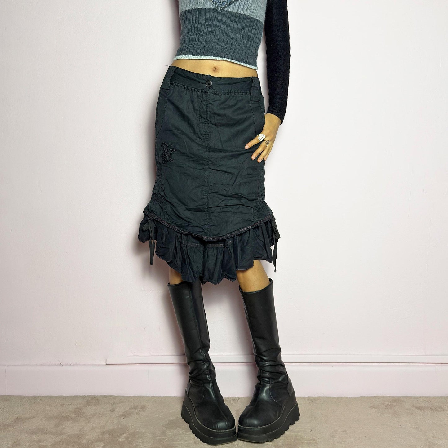 The Y2K Black Layered Skirt by Marithé François Girbaud is a vintage 2000s statement piece featuring a structured design with ruched details and ruffled layers for added texture and movement. Designed with a mid-rise fit, button and zipper closure, embroidered side detail, and an asymmetrical hem, this skirt blends edgy streetwear vibes with a playful, gothic aesthetic. Perfect for casual grunge and alternative looks. adult world shop