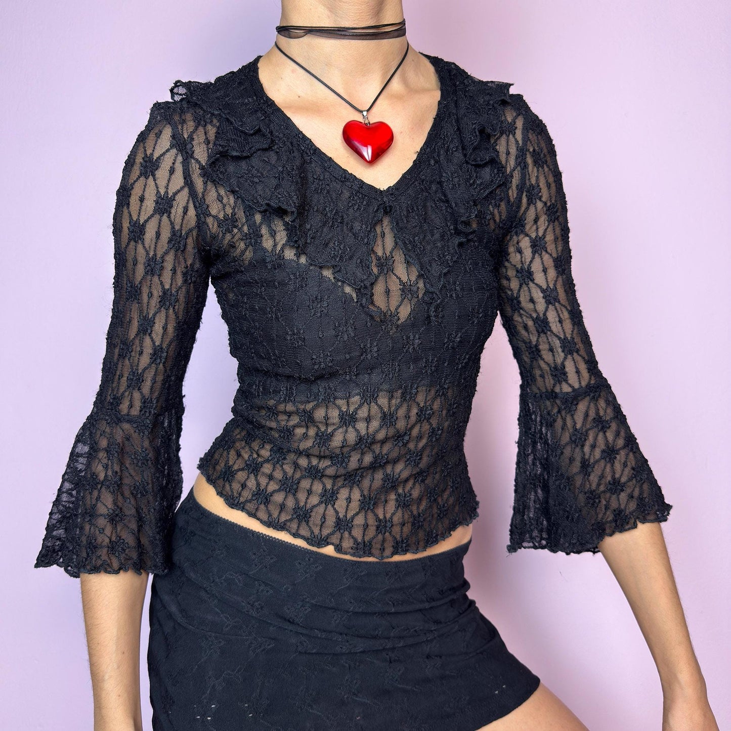 The Y2K Lace Ruffle Black Top is a vintage 2000s sheer black lace top featuring a fitted silhouette, mini ruffle details along the neckline, and flared three-quarter bell sleeves. The textured floral lace adds a romantic gothic touch, perfect for layering or wearing on its own. Ideal for summer night looks and festival outfits. Great vintage condition. adult world shop