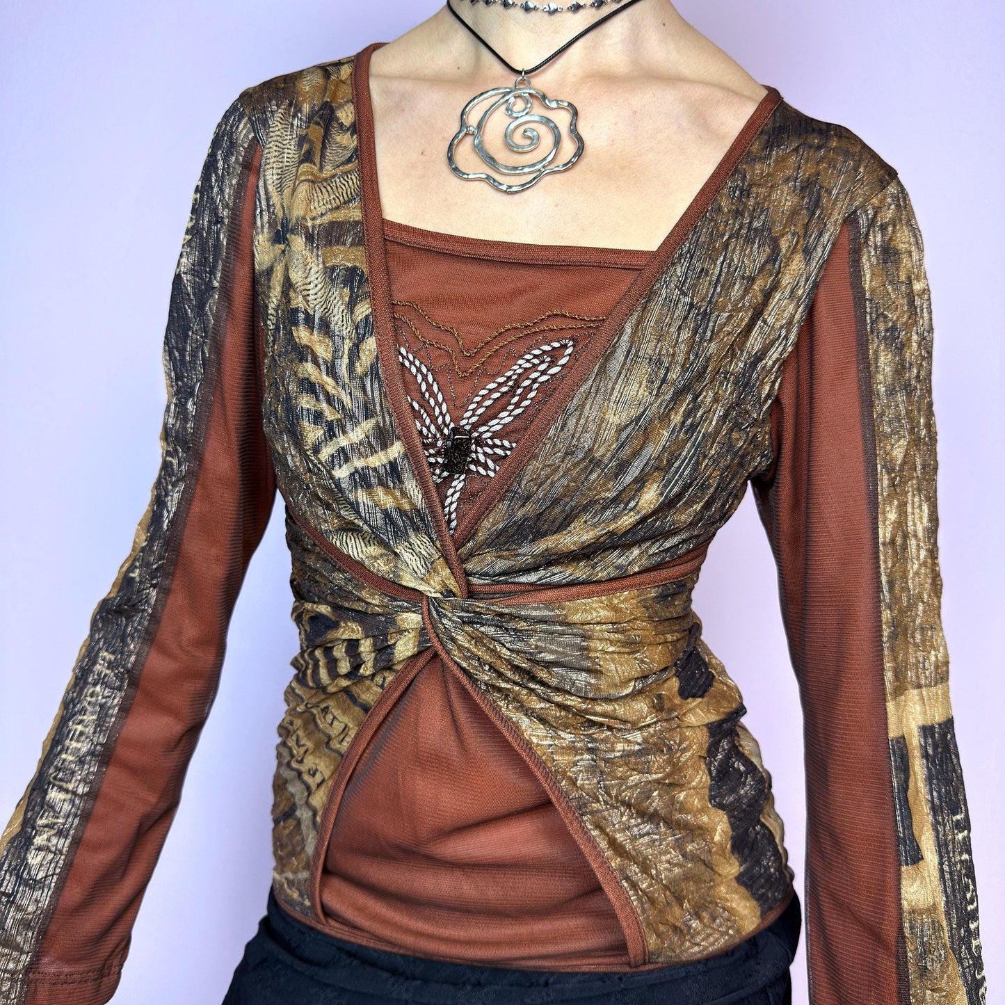 The Y2K Brown Mesh Overlay Top is a vintage 2000s long sleeve designed by Legatte Jeans. Crafted in a moody mix of orange, brown, and bronze tones, it features a twisted front detail and a combination of stretchy mesh and jersey fabrics. A subtle embroidered flower motif decorates the chest, adding a delicate accent to the bold, structured silhouette. With its sculptural cut and sheer elements, this top is perfect for cyber aesthetics, artsy fashion, and Y2K clubwear. adult world shop