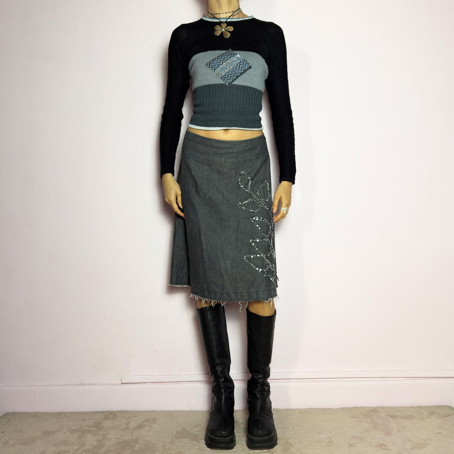 The Y2K Denim Gray Midi Skirt is a vintage 2000s piece featuring a faded gray wash, raw hem, and a unique floral sequin embroidery design. Crafted from structured denim, this skirt has an A-line silhouette that drapes effortlessly. Designed with a back zipper closure, the unfinished hem adds a deconstructed, edgy touch, making it perfect for casual outfits. adult world shop