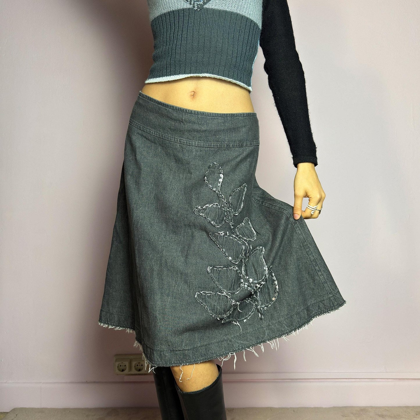 The Y2K Denim Gray Midi Skirt is a vintage 2000s piece featuring a faded gray wash, raw hem, and a unique floral sequin embroidery design. Crafted from structured denim, this skirt has an A-line silhouette that drapes effortlessly. Designed with a back zipper closure, the unfinished hem adds a deconstructed, edgy touch, making it perfect for casual outfits. adult world shop