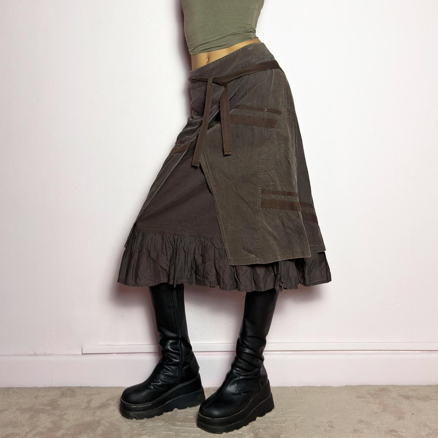 The Y2K Layered Brown Midi Skirt is a unique vintage 2000s piece featuring an asymmetric wrap design with a layered ruffle hem. Made from corduroy-cotton fabric, it includes tie closures for an adjustable fit, a back zipper closure, and subtle stitched detailing that adds a deconstructed touch. Perfect for earthy, bohemian, or avant-garde styling. adult world shop