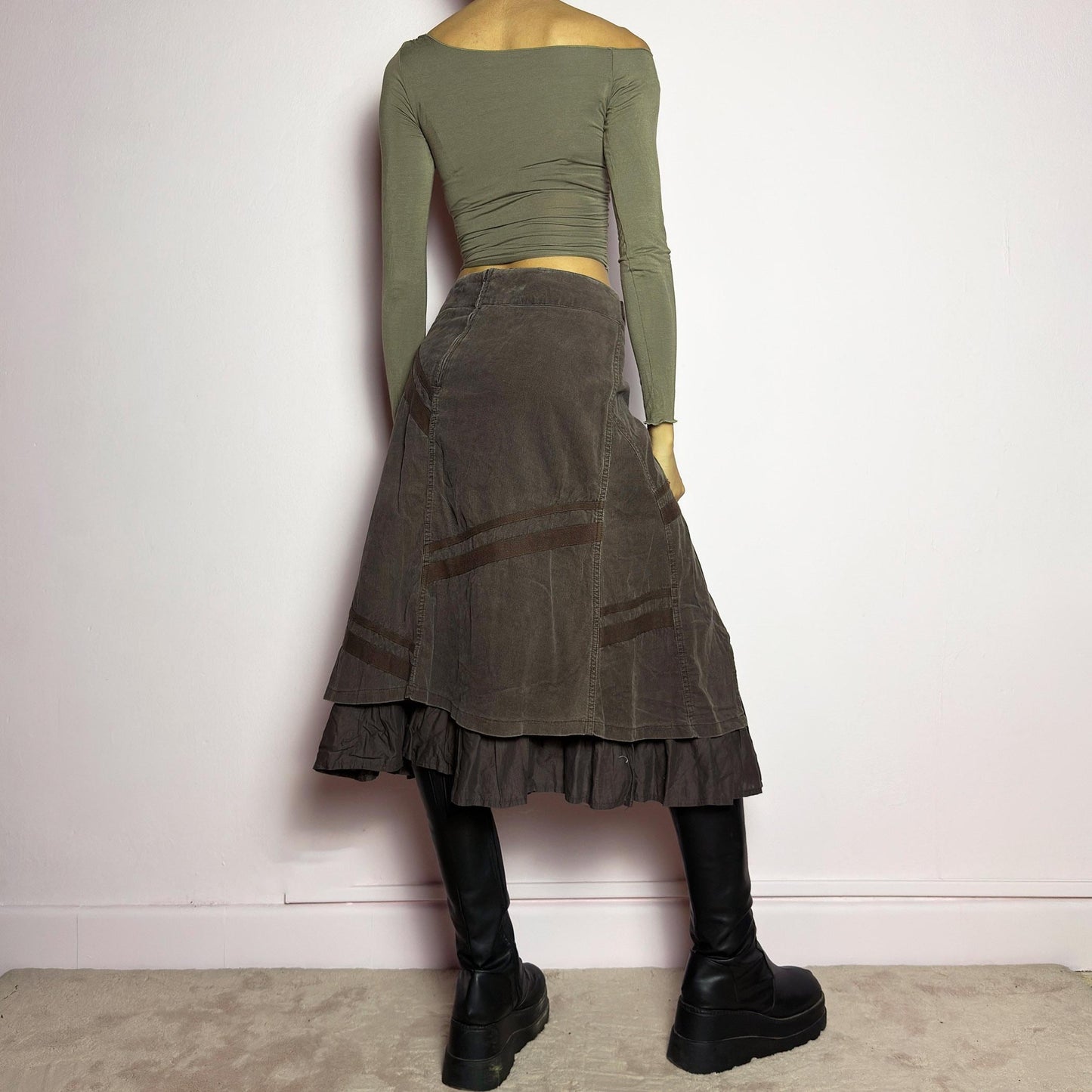 The Y2K Layered Brown Midi Skirt is a unique vintage 2000s piece featuring an asymmetric wrap design with a layered ruffle hem. Made from corduroy-cotton fabric, it includes tie closures for an adjustable fit, a back zipper closure, and subtle stitched detailing that adds a deconstructed touch. Perfect for earthy, bohemian, or avant-garde styling. adult world shop
