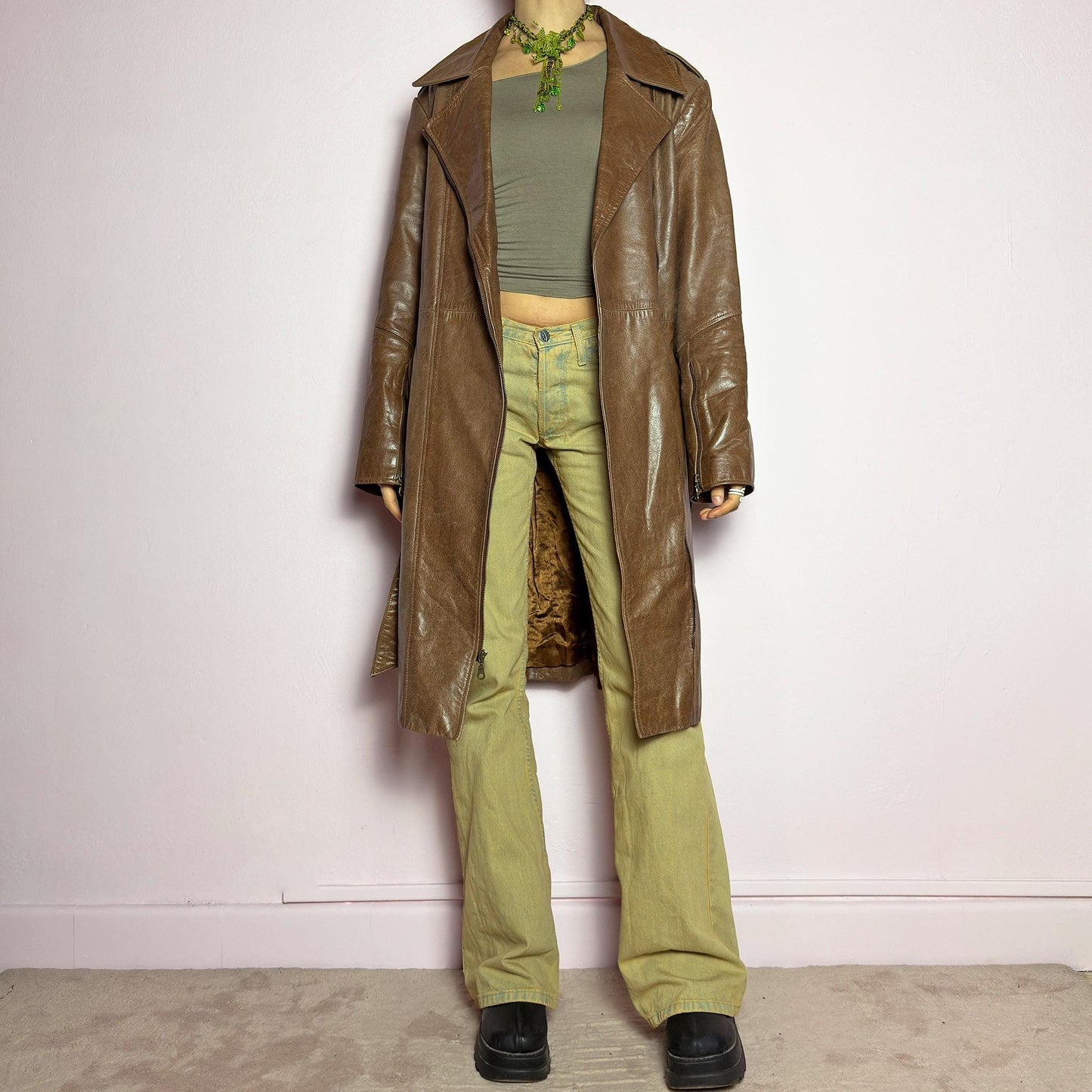 The Y2K Long Brown Leather Coat is a heavy, structured vintage 2000s piece crafted from genuine leather. It features an asymmetrical zip closure, a wide lapel collar, and a belted waist for a cinched silhouette. The coat includes pockets and a smooth lining for comfort. With its durable construction and timeless design, this vintage long leather coat is perfect for edgy streetwear or sophisticated layering. adult world shop