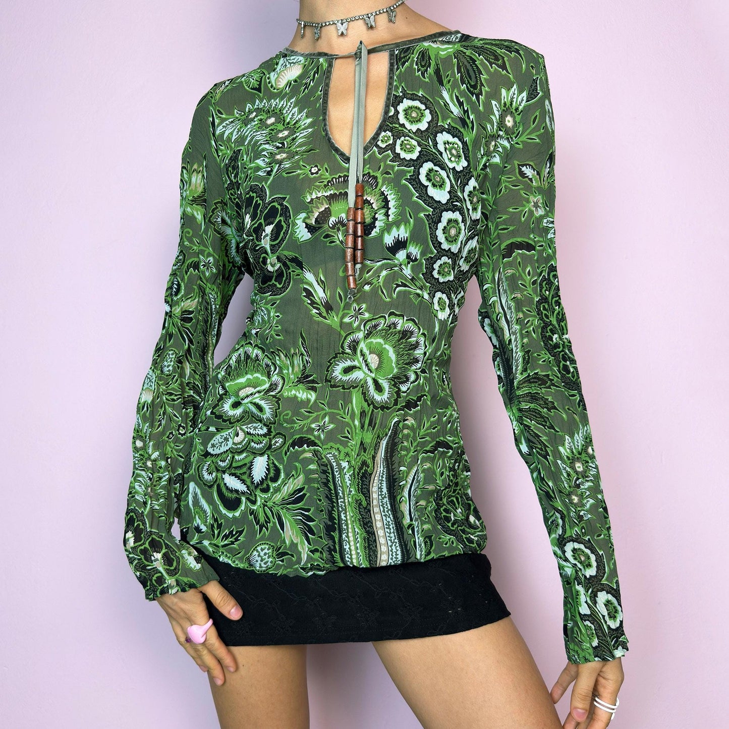 The Y2K Green Boho Tie Front Top is a vintage 2000s piece featuring an abstract floral print on lightweight, semi-sheer fabric. Designed with a front keyhole neckline and adjustable tie adorned with wooden bead details. The long sleeves and breathable material make it comfy and flattering. A unique top perfect for summer layering, festival outfits, fairy grunge, or earthy boho styles.