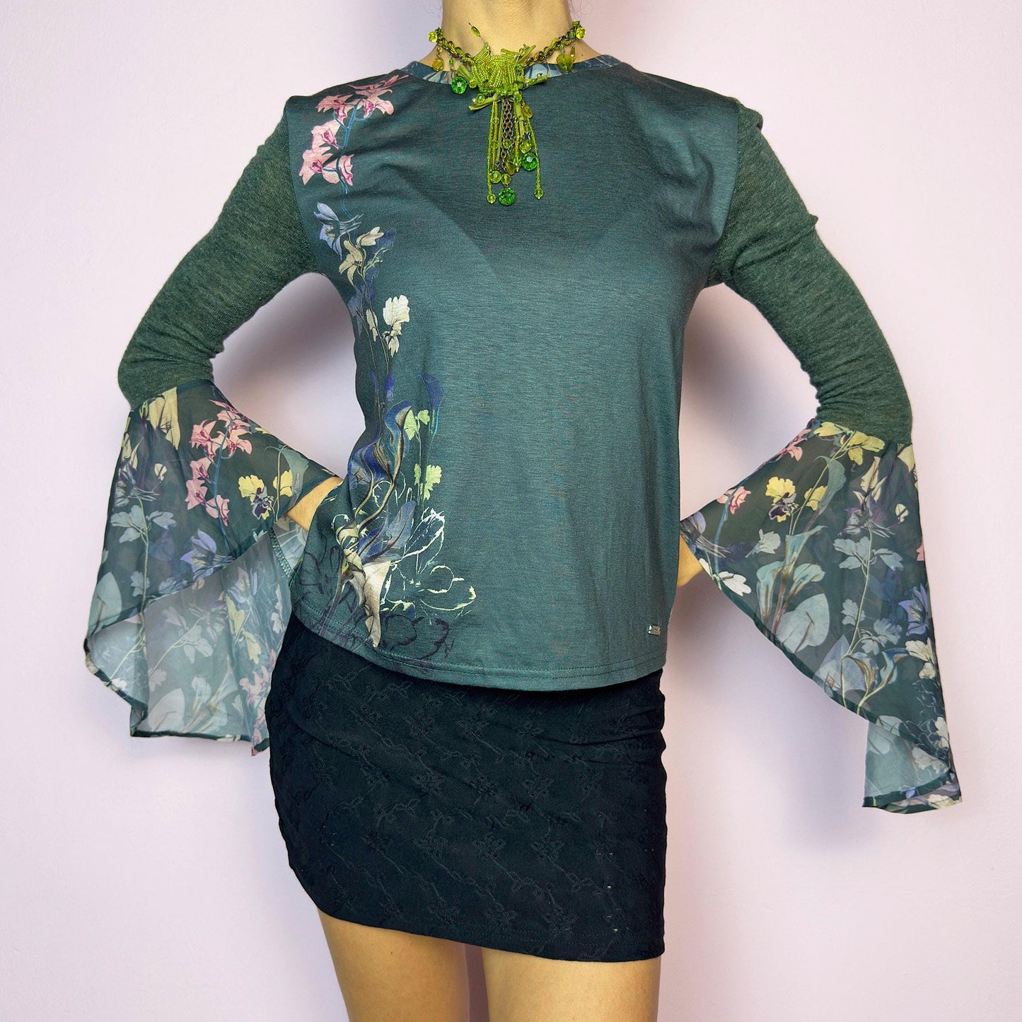 The Y2K Green Bell Sleeve Top is a rare vintage 2000s piece with ethereal vibes. Features stretchy semi-sheer forest green fabric with a romantic floral print on one side and dramatic bell sleeves adorned with matching botanical motifs. Soft and lightweight. Perfect for fairycore and festival looks. Great vintage condition.