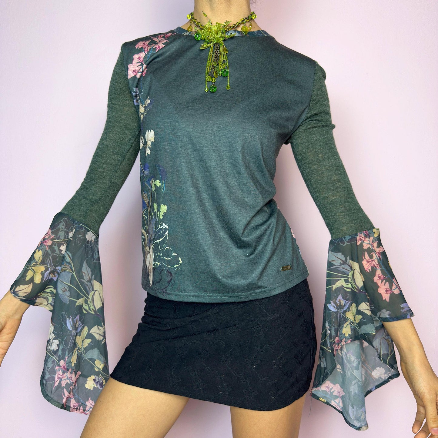 The Y2K Green Bell Sleeve Top is a rare vintage 2000s piece with ethereal vibes. Features stretchy semi-sheer forest green fabric with a romantic floral print on one side and dramatic bell sleeves adorned with matching botanical motifs. Soft and lightweight. Perfect for fairycore and festival looks. Great vintage condition.