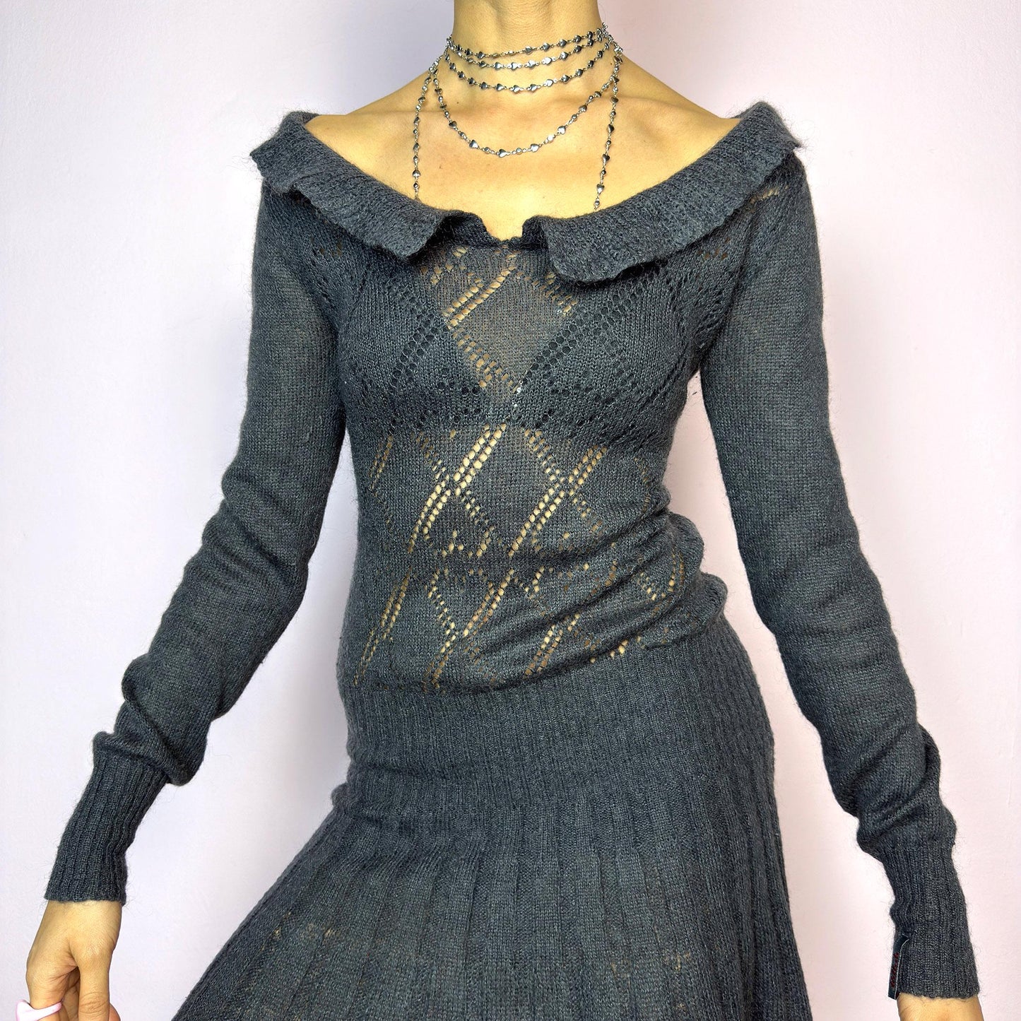 The Y2K Gray Mini Knit Dress is a vintage 2000s piece featuring a ruffled off-shoulder neckline and sheer diamond-knit pattern through the bodice. The fitted waist flows into a pleated mini skirt. Made from a soft, stretchy knit that hugs the body while remaining comfortable. Perfect for casual autumn look. adult world shop
