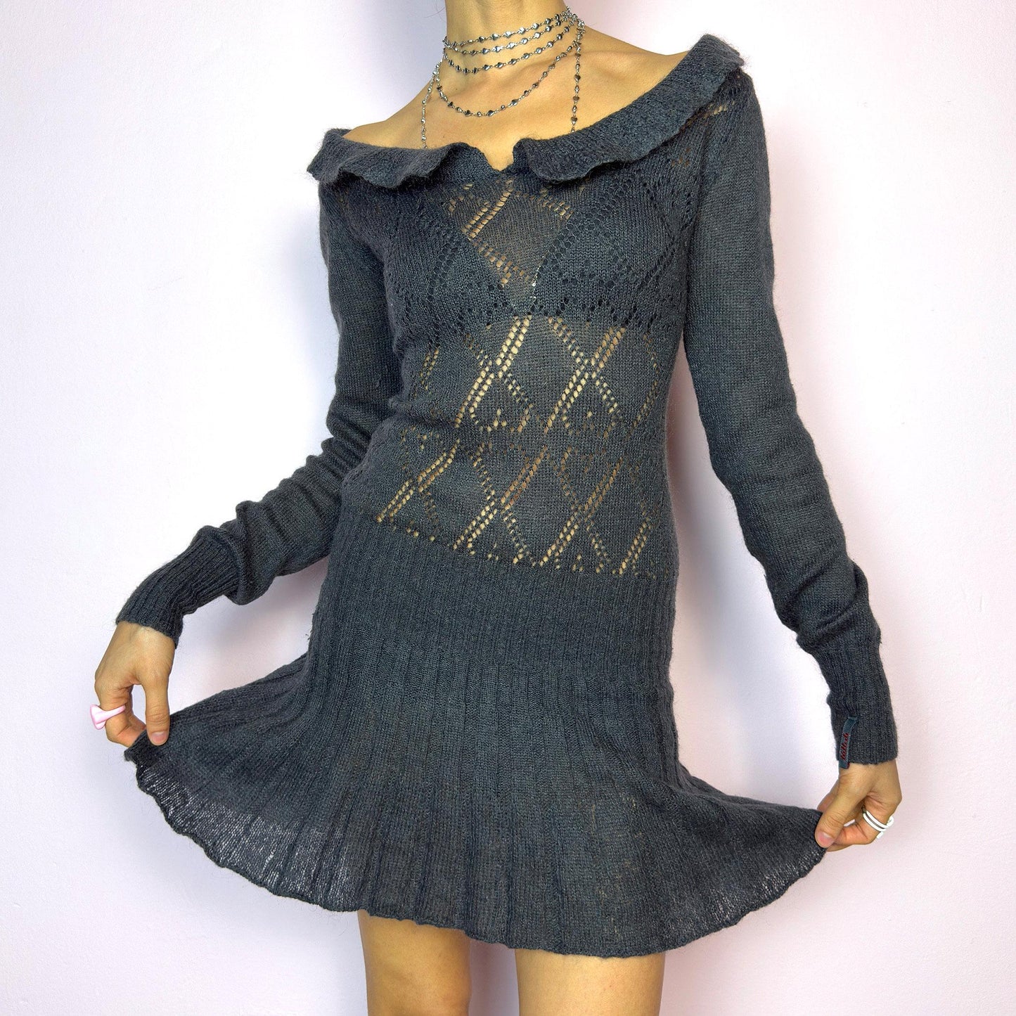 The Y2K Gray Mini Knit Dress is a vintage 2000s piece featuring a ruffled off-shoulder neckline and sheer diamond-knit pattern through the bodice. The fitted waist flows into a pleated mini skirt. Made from a soft, stretchy knit that hugs the body while remaining comfortable. Perfect for casual autumn look. adult world shop