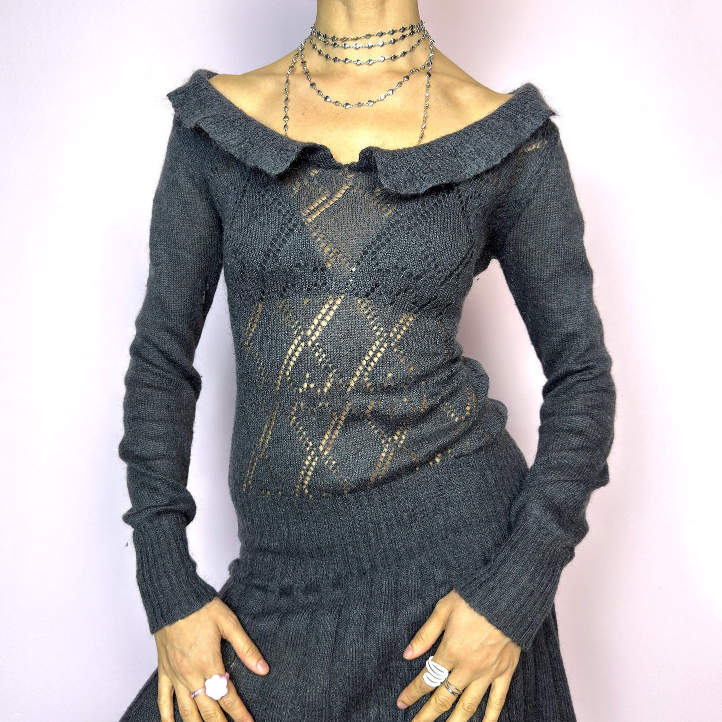 The Y2K Gray Mini Knit Dress is a vintage 2000s piece featuring a ruffled off-shoulder neckline and sheer diamond-knit pattern through the bodice. The fitted waist flows into a pleated mini skirt. Made from a soft, stretchy knit that hugs the body while remaining comfortable. Perfect for casual autumn look. adult world shop
