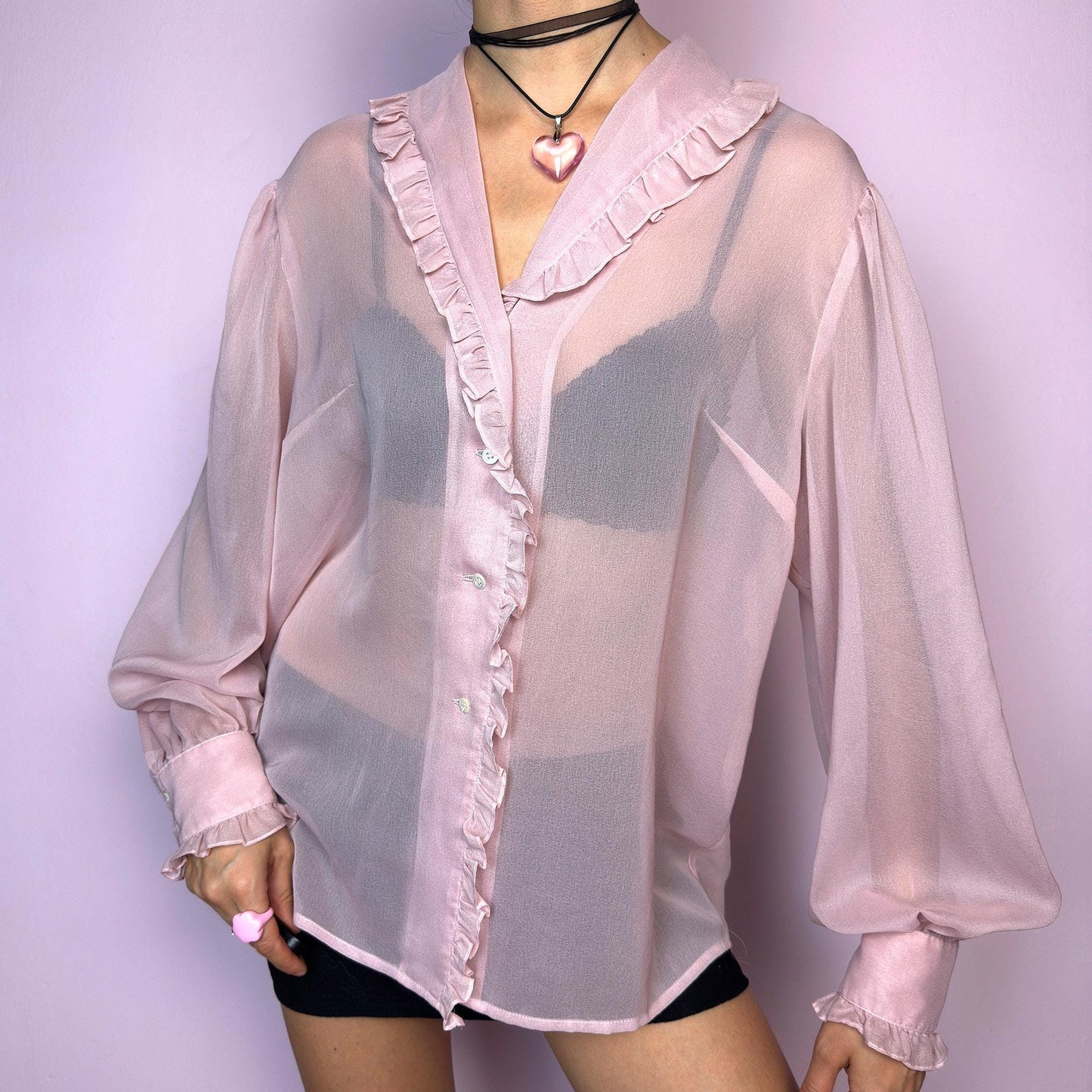 The Vintage Pink Ruffle Sheer Blouse features a romantic and ethereal silhouette with soft, see-through fabric and delicate ruffle trim along the collar and button placket. The flowy cut and voluminous sleeves with buttoned cuffs add a dreamy charm. Perfect for layering for a soft coquette aesthetic. Made in France. Excellent vintage condition. adult world shop